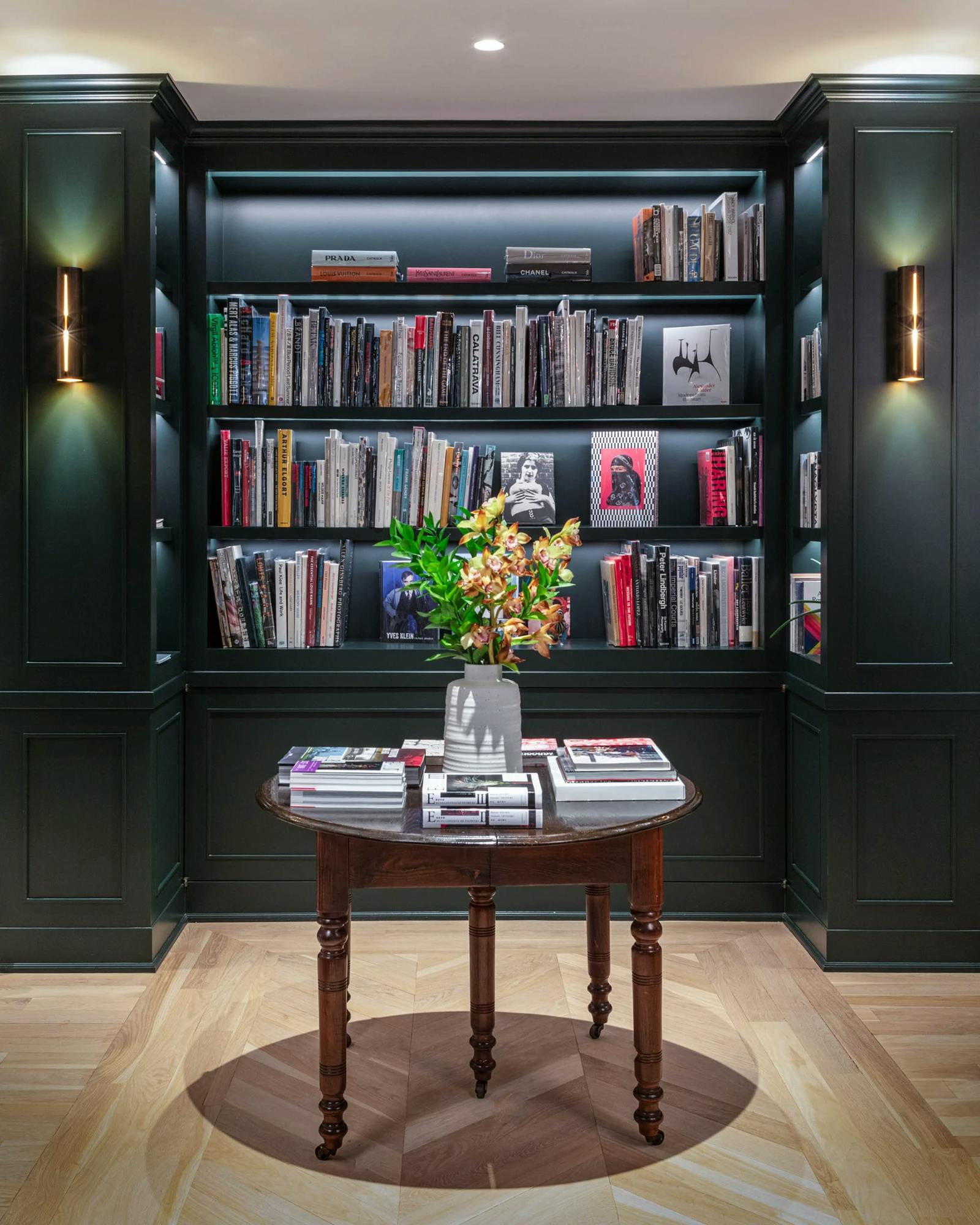 A dark green library nook with books at FIG behind a small circular table with a bouquet of flowers on top.