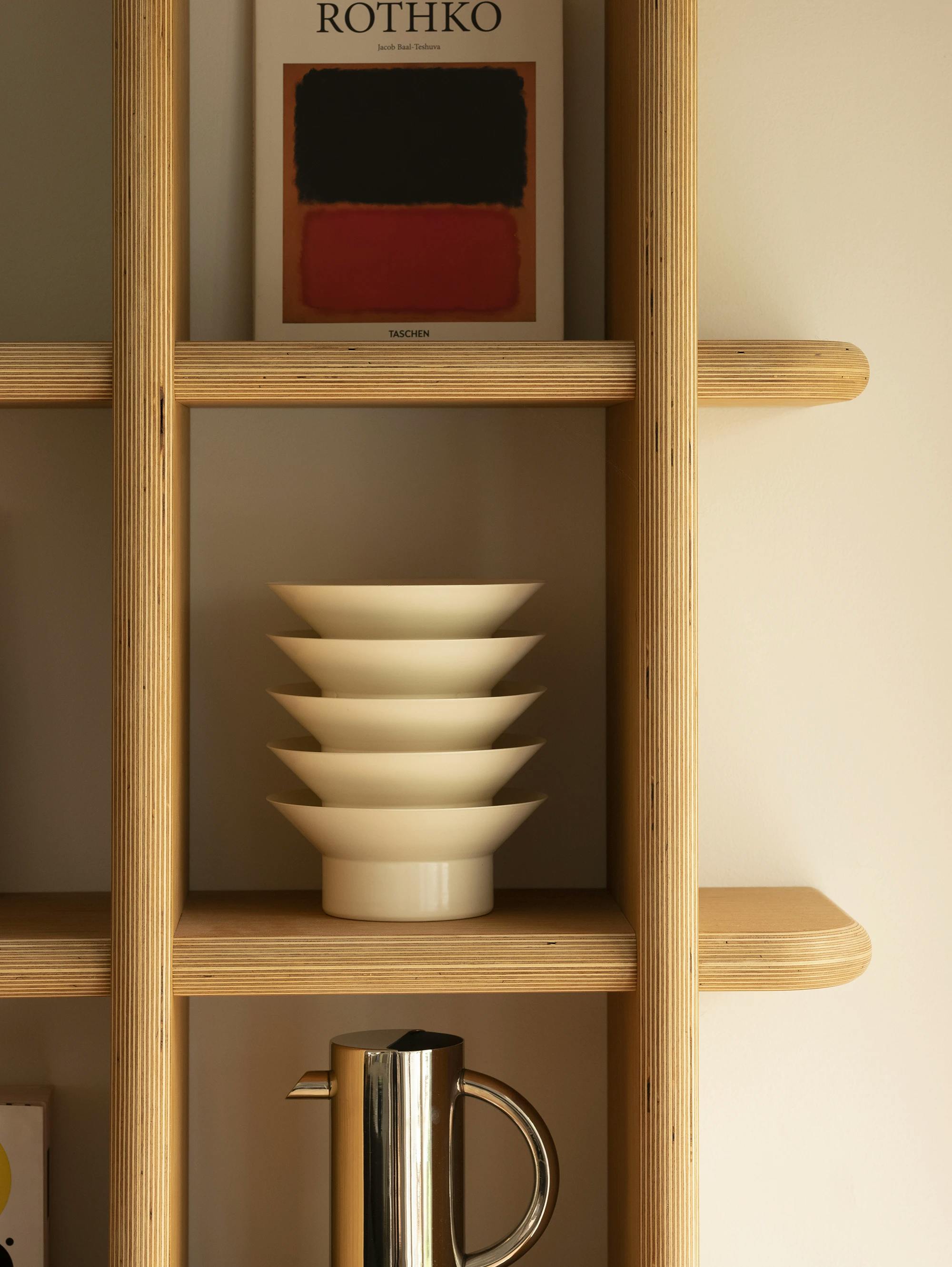 A stack of bowls on a wooden bookshelf. 