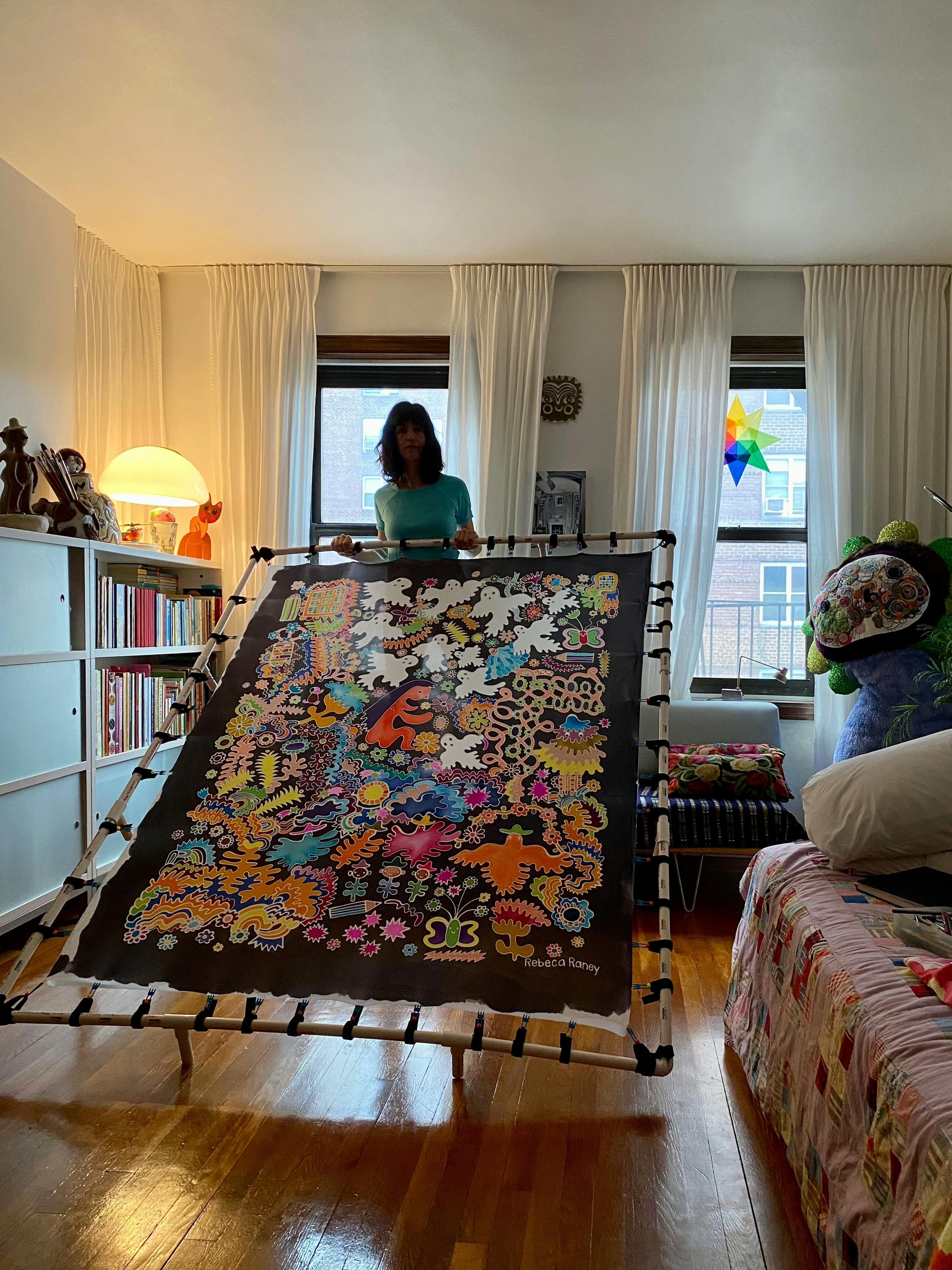 Artist Rebeca Raney holding up a stretched artwork on silk in her home studio.