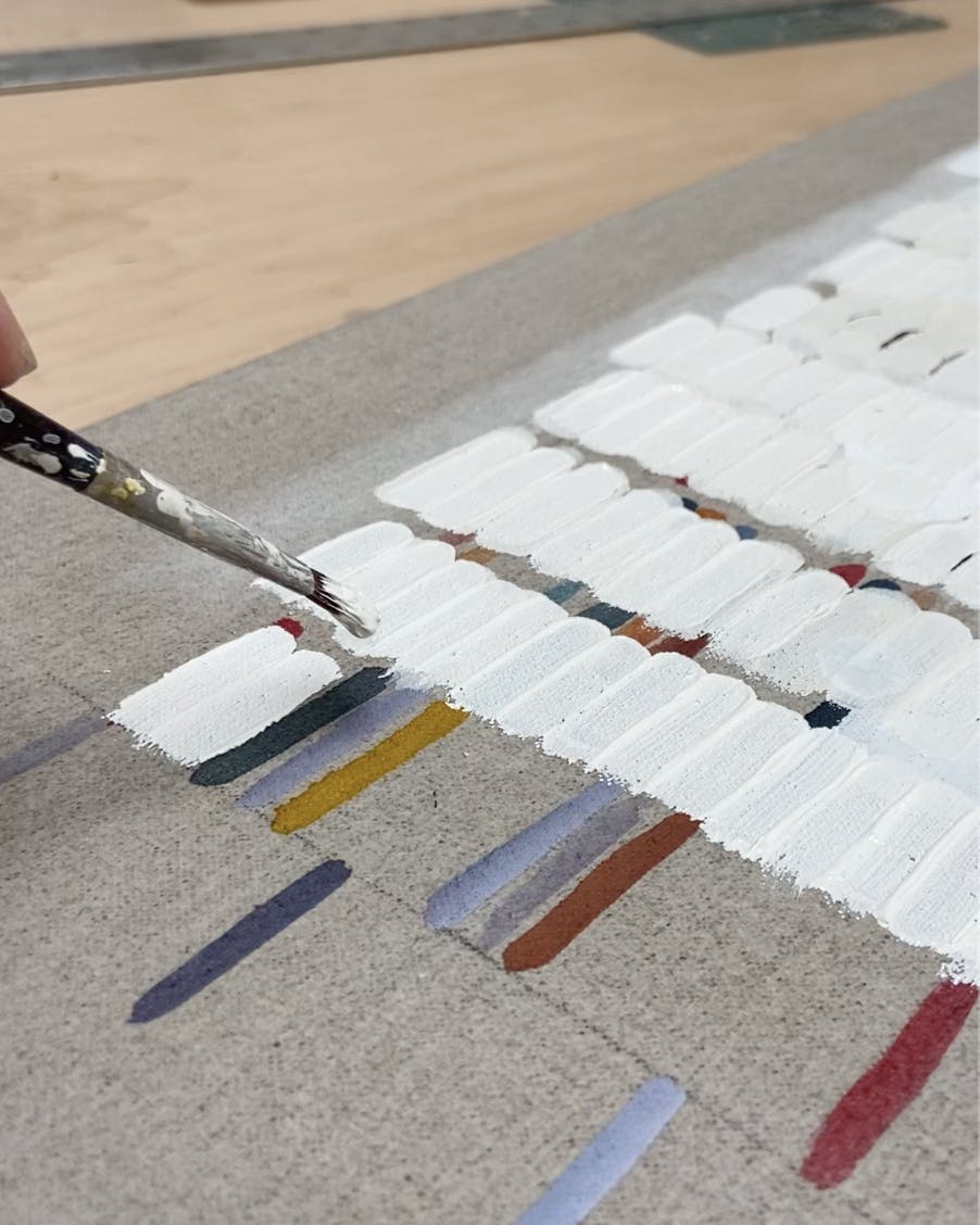 Close-up of artist Gail Tarantino painting white lines on a grey linen canvas.