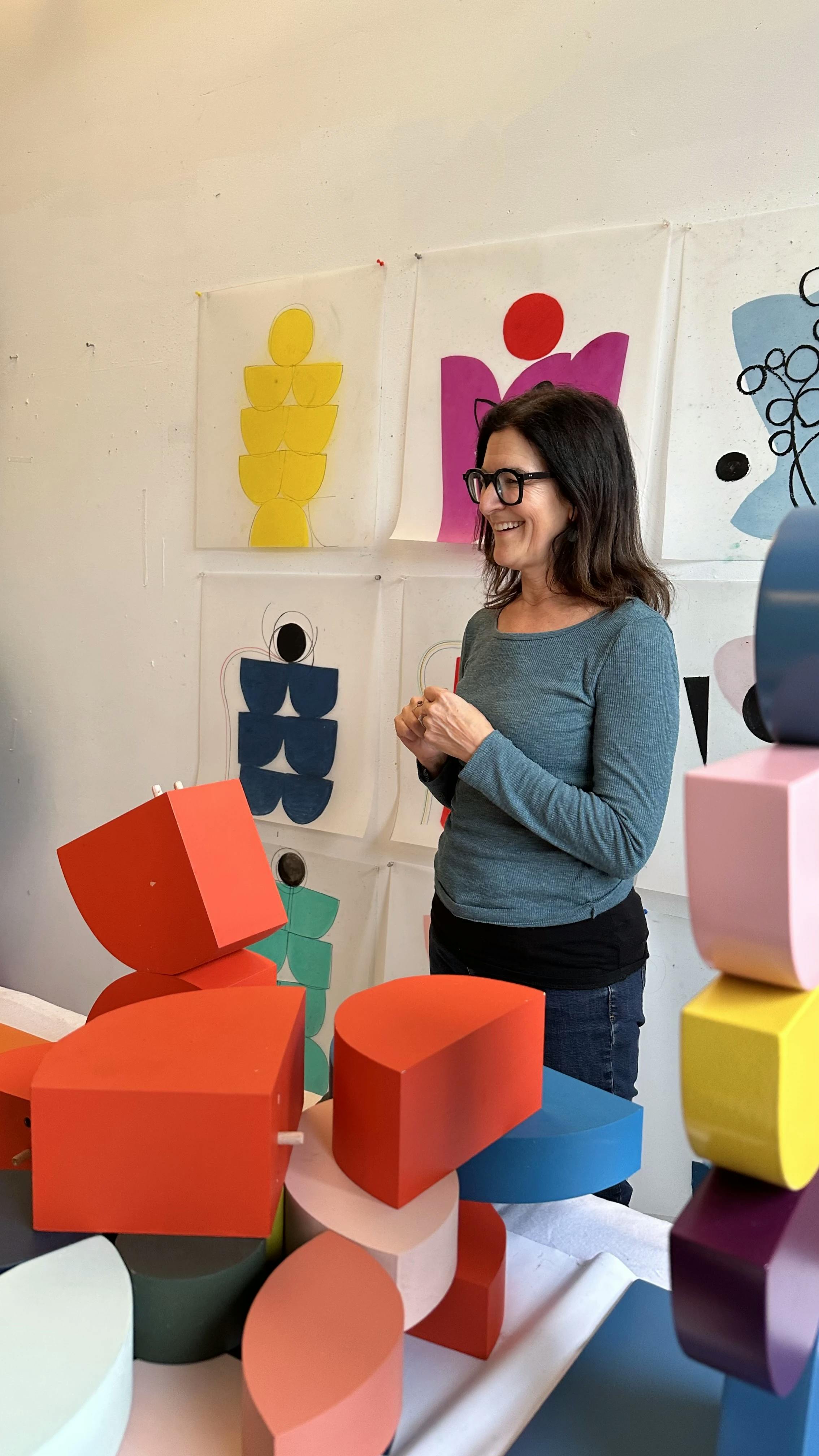 Artist Vicki Sher standing next to a pile of colorful, aluminum sculpture pieces.