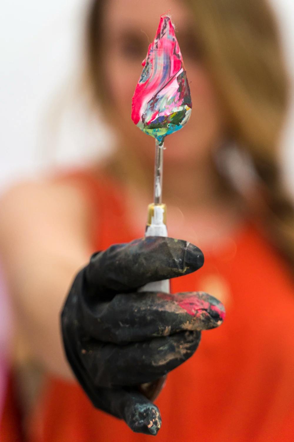 Artist Erin Lynn Welsh holding up a palette knife covered in colorful paint. 