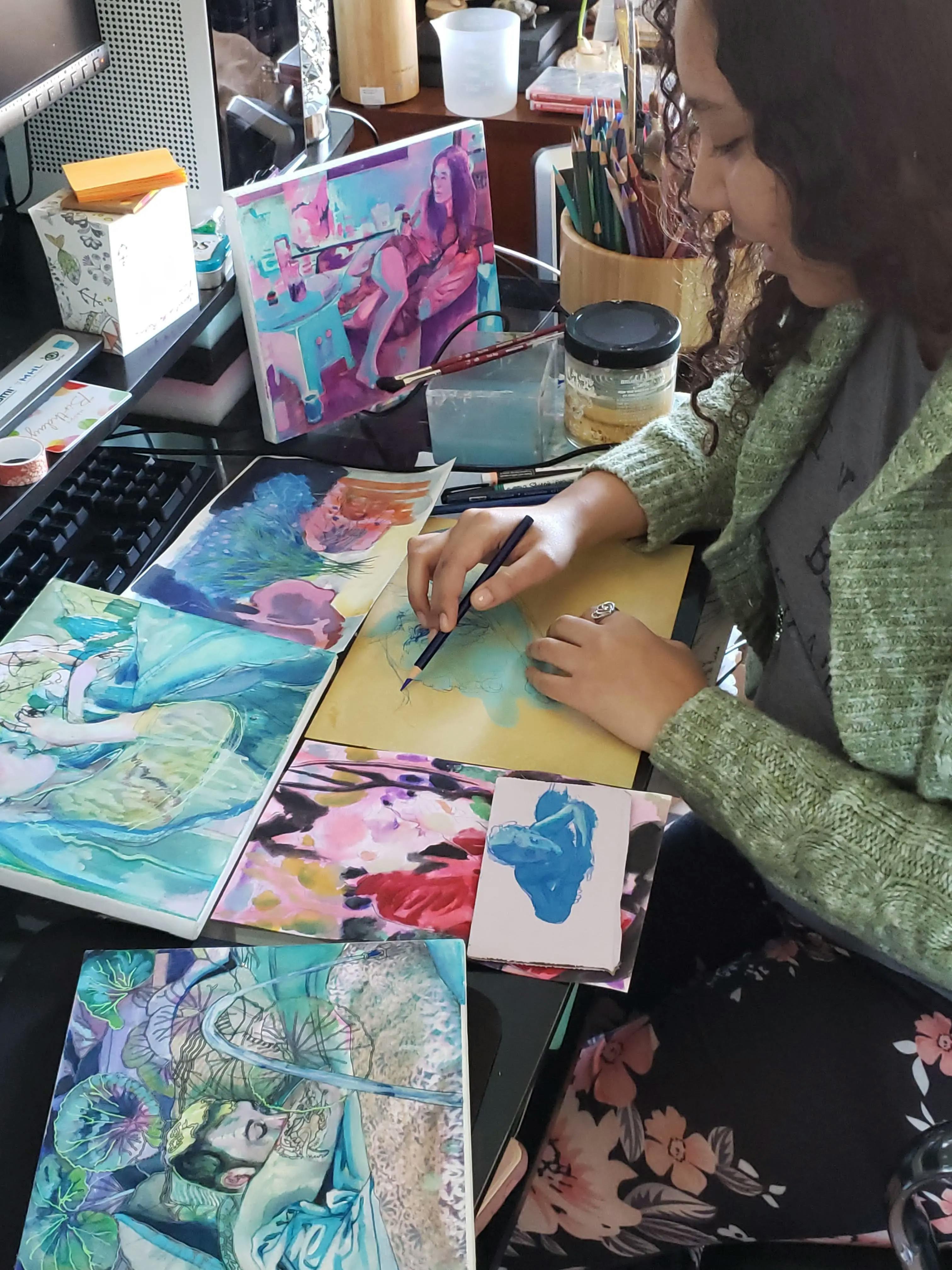Artist Nefertiti Jenkins at a desk in her studio surrounded by her own paintings, using a pencil to draw an outline on an in-progress composition.