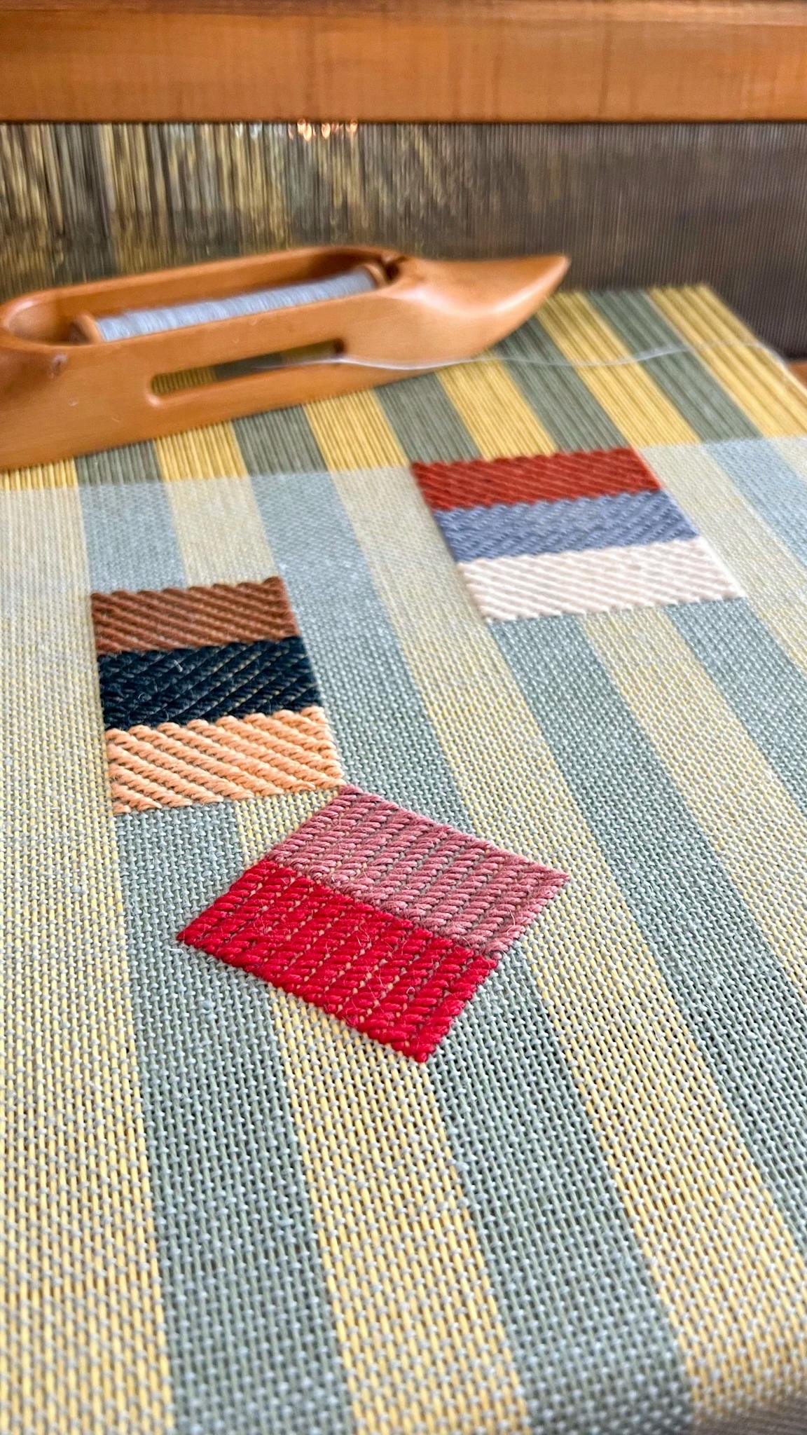 A close-up of a striped artwork by Sarah Sullivan Sherrod with a loom in the background.