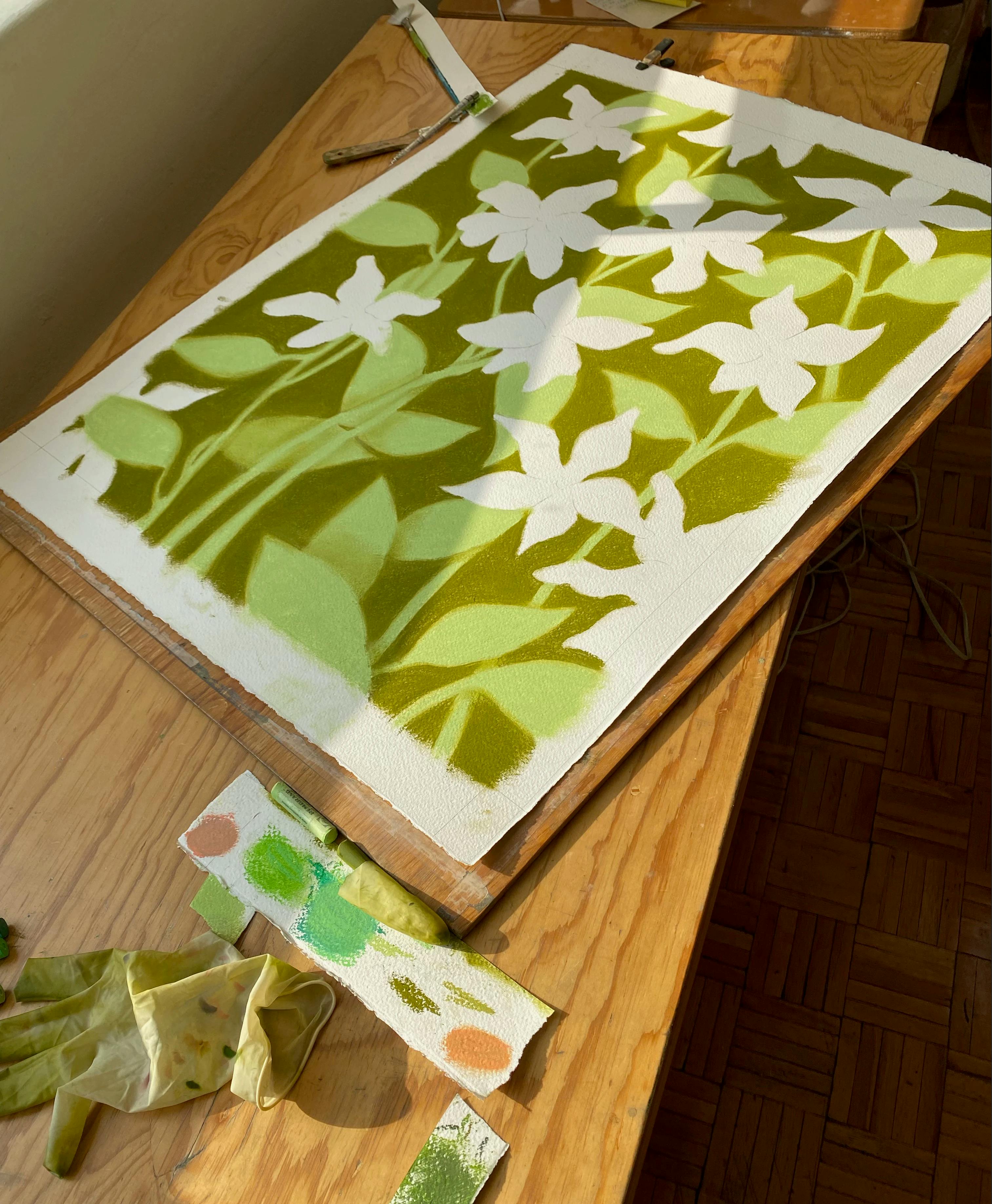 Pastel drawing with green leaves and white flowers by artist Rachel Levit Ruiz on a wooden table in her studio.