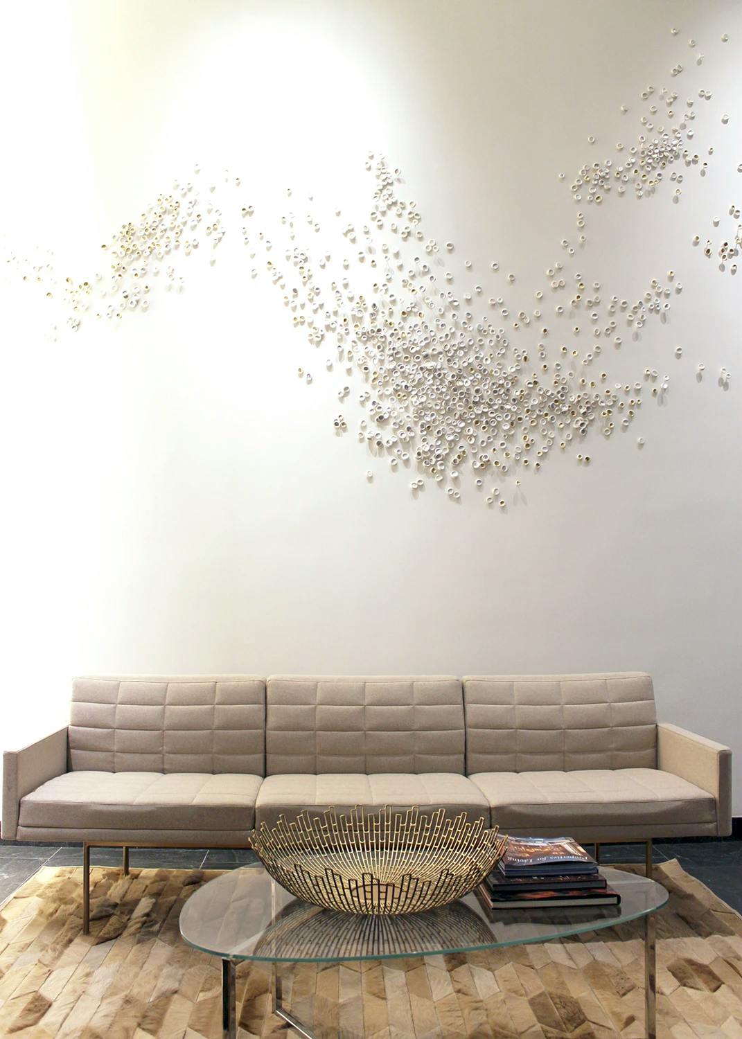 A custom porcelain installation by artist Christina Watka above a beige sofa in the lounge area of a modern residential building.