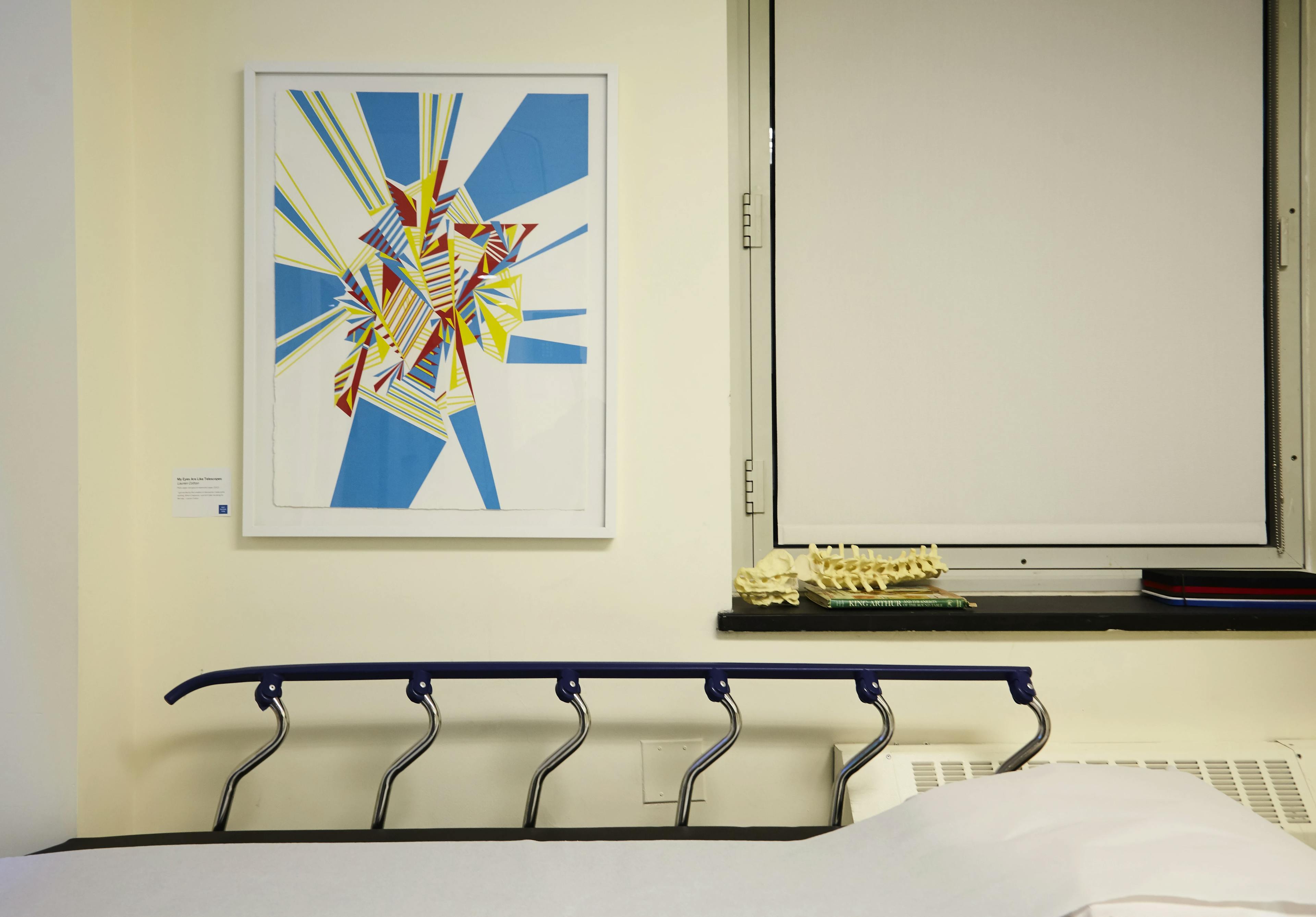 Multicolored, geometric abstract collage on paper installed above a hospital bed with railings.