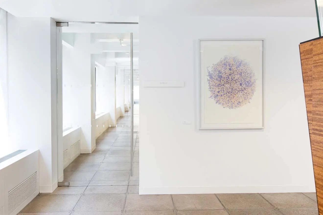 Framed artwork with purple abstract circle installed on a white wall in the hallway of a modern office building with glass doors.