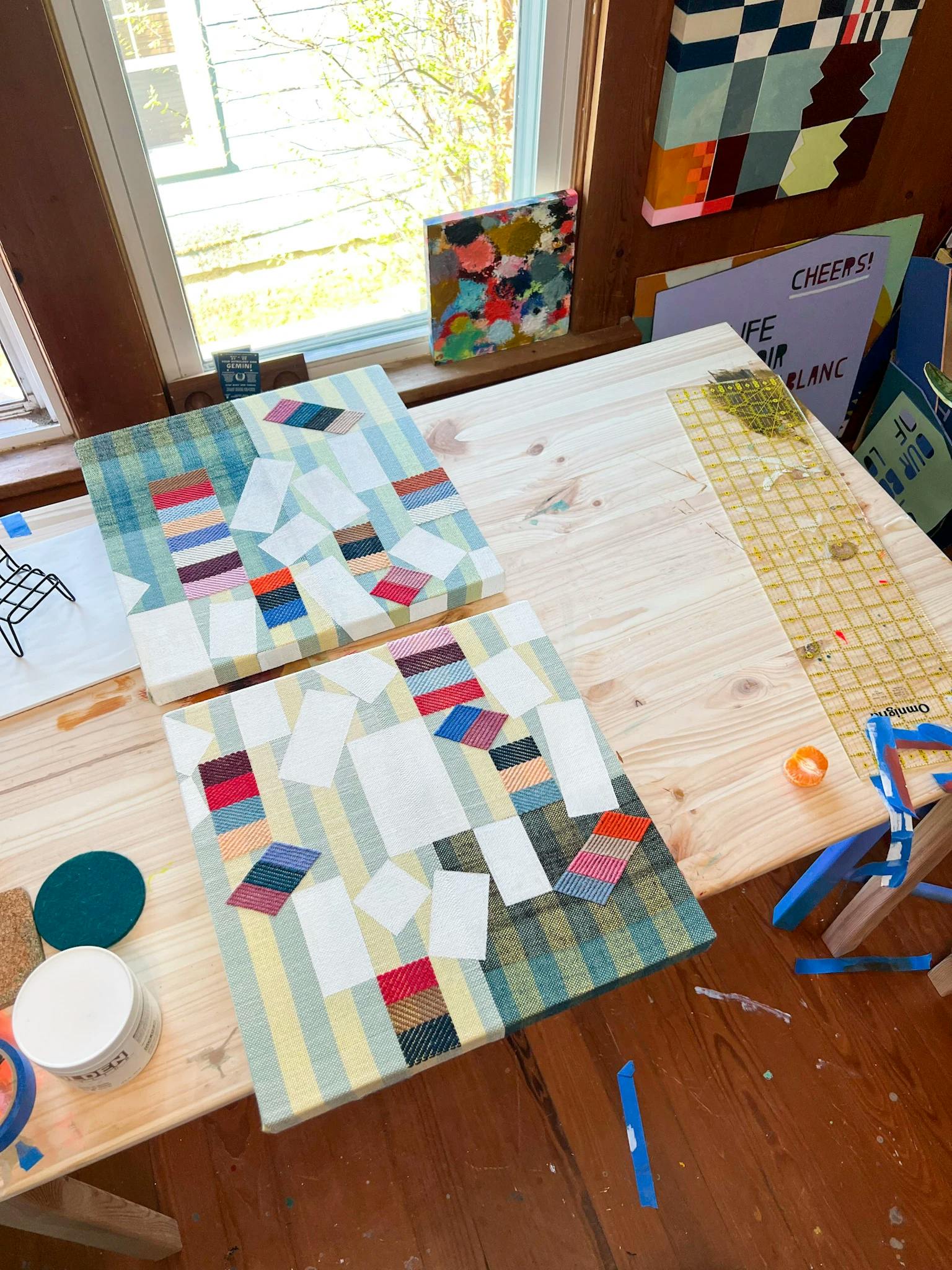 An aerial view of two striped, woven and painted pieces by artist Sarah Sullivan Sherrod on a wooden table in her light-filled studio.