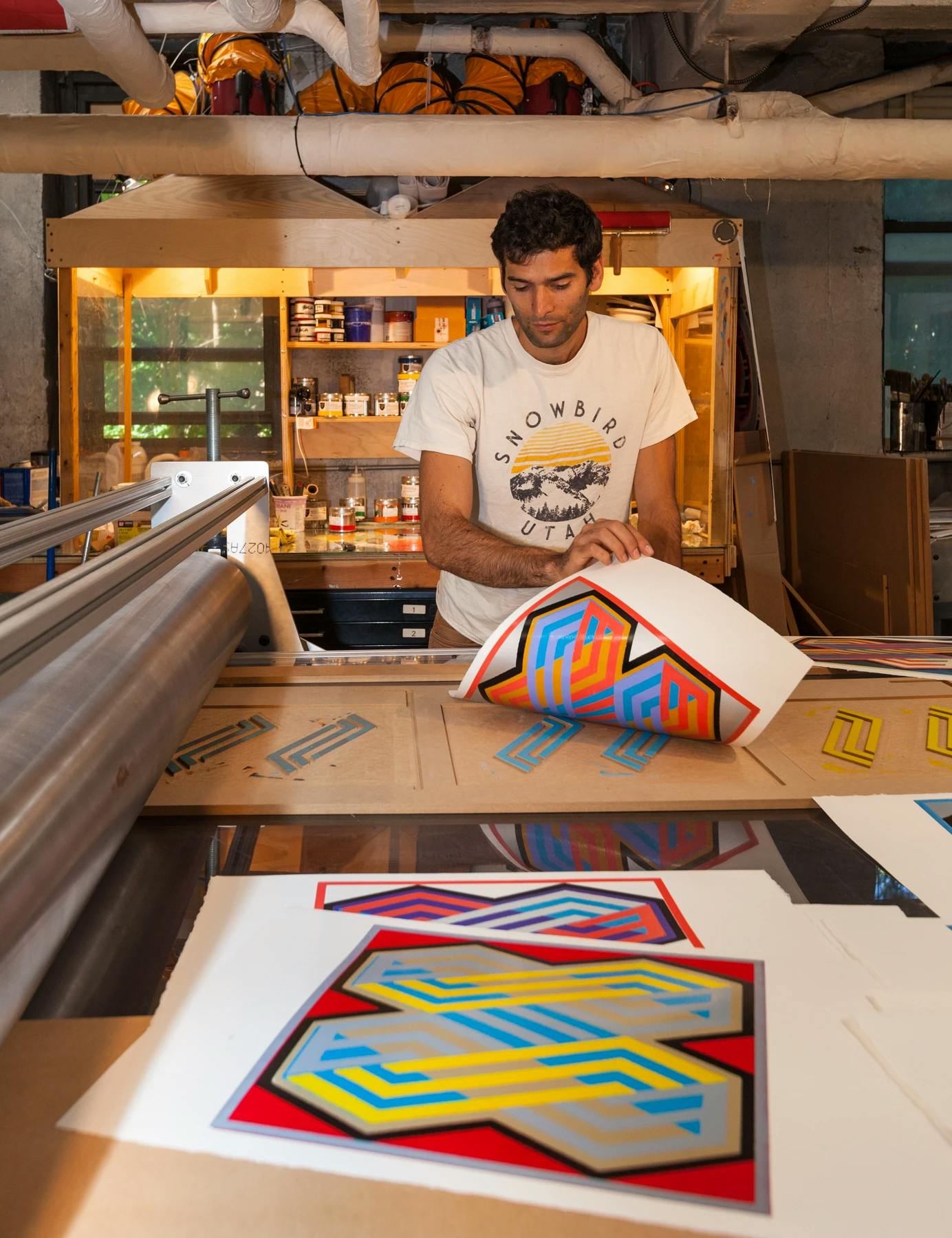 Artist Matt Neuman wearing a white t-shirt creating geometric, abstract prints in his studio.