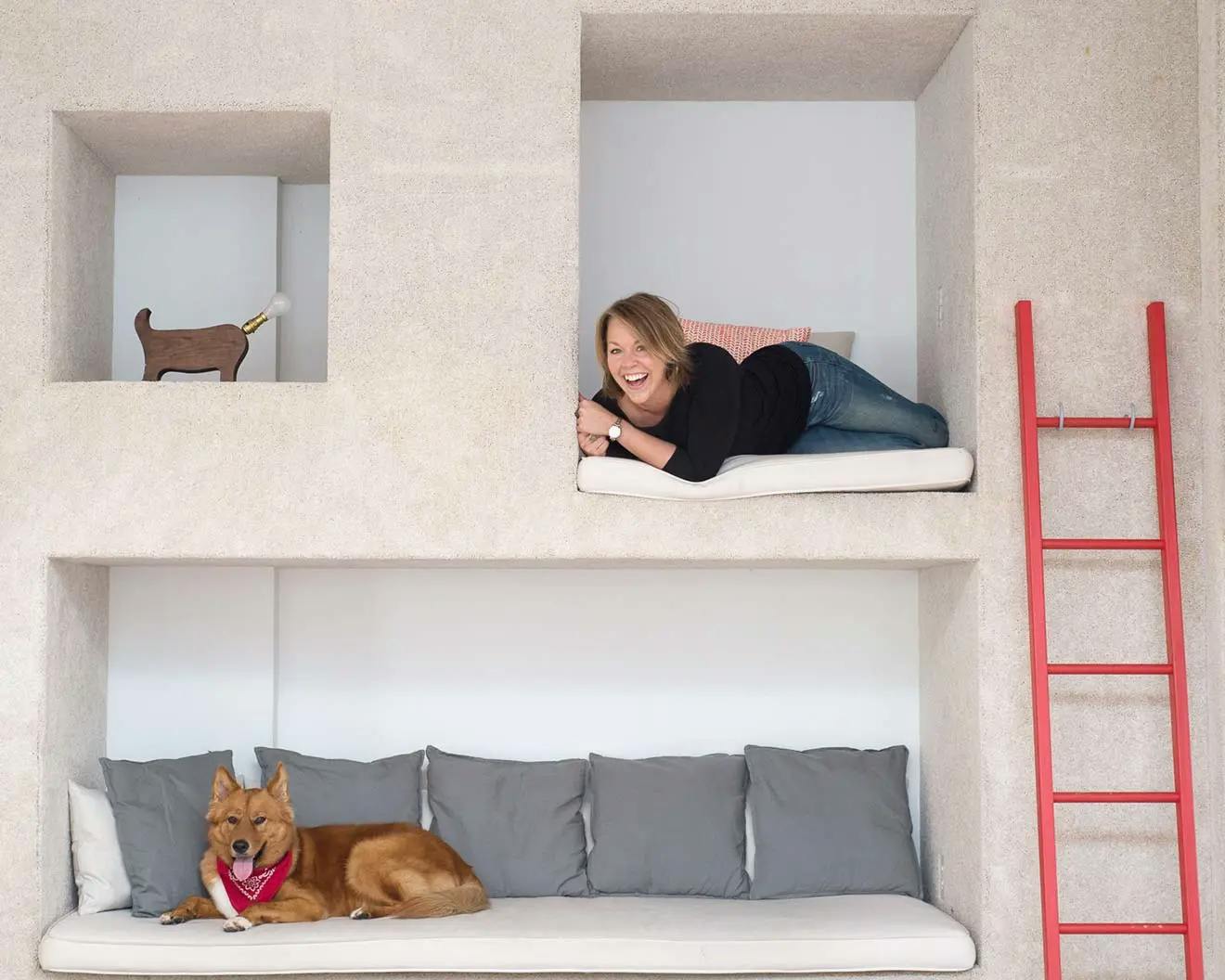 Artist Christina Watka laying in an alcove above another alcove with a dog with a red bandana.