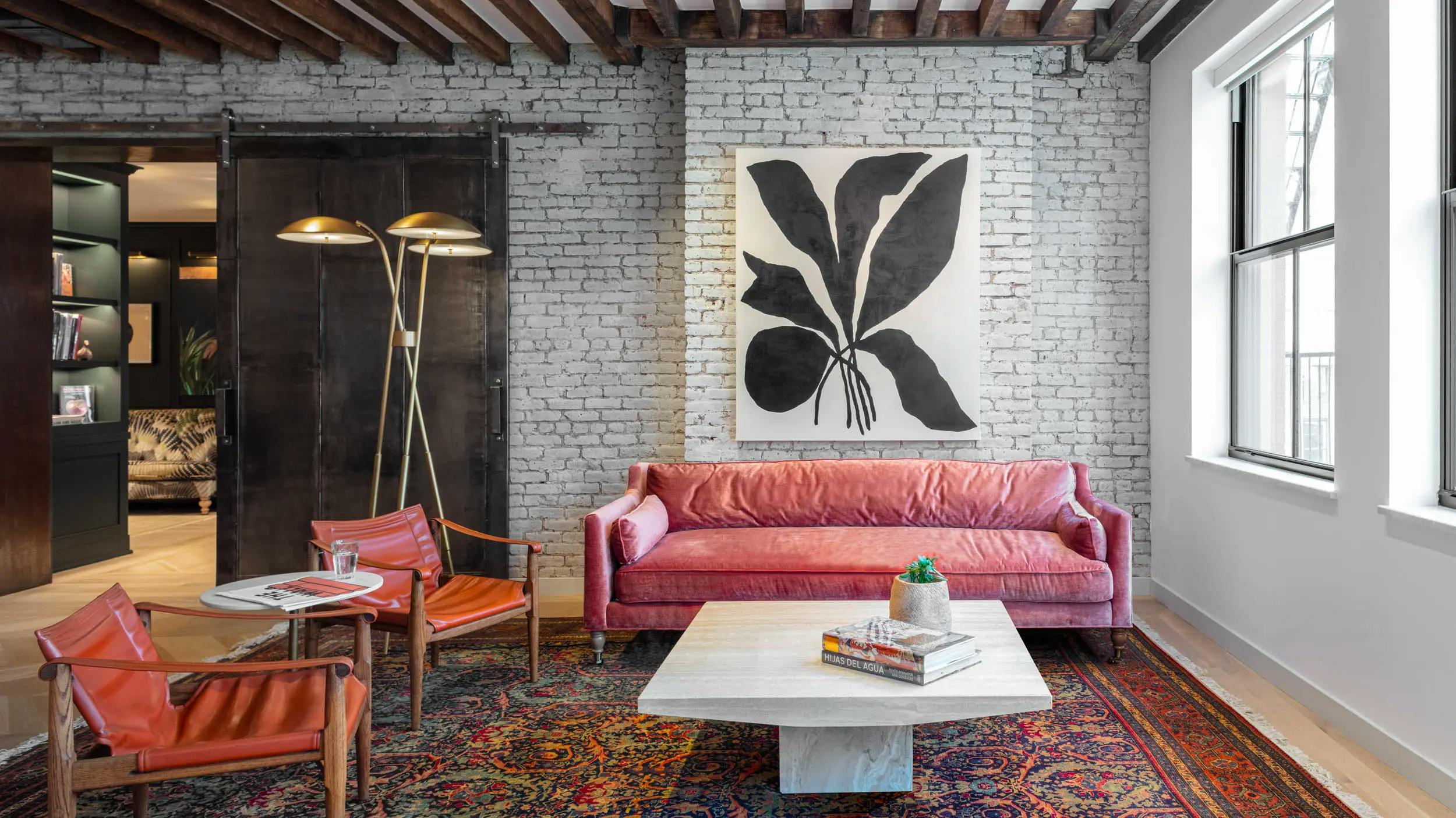 The lounge area at FIG featuring a patterned rug, two red chairs, and a large black and white botanical painting by artist Kate Roebuck on a white brick wall above a pink sofa.