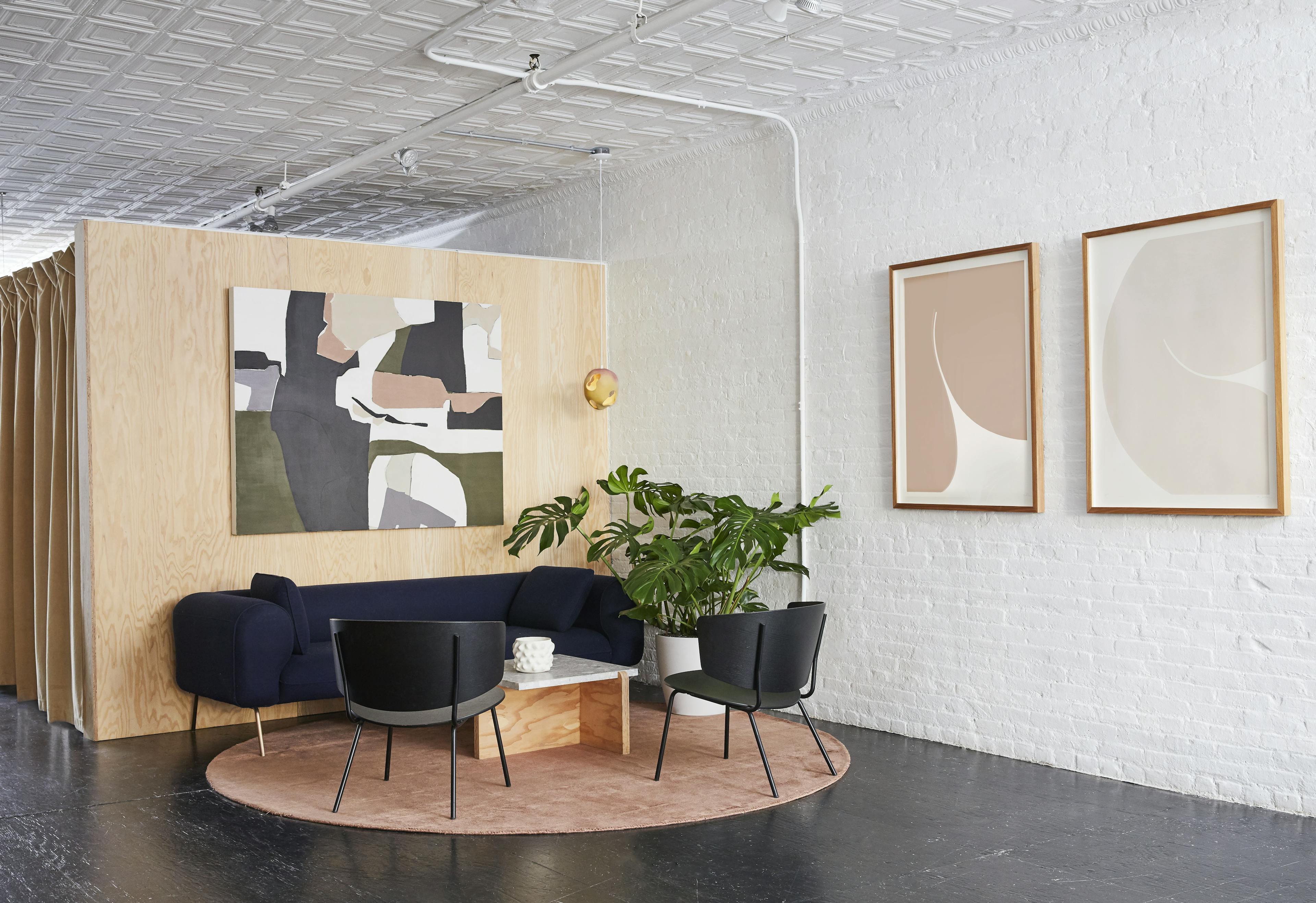 A wood wall intersects a white brick wall to create the lounge area at Uprise Art, complete with a navy couch and black chairs on a red circular rug.
