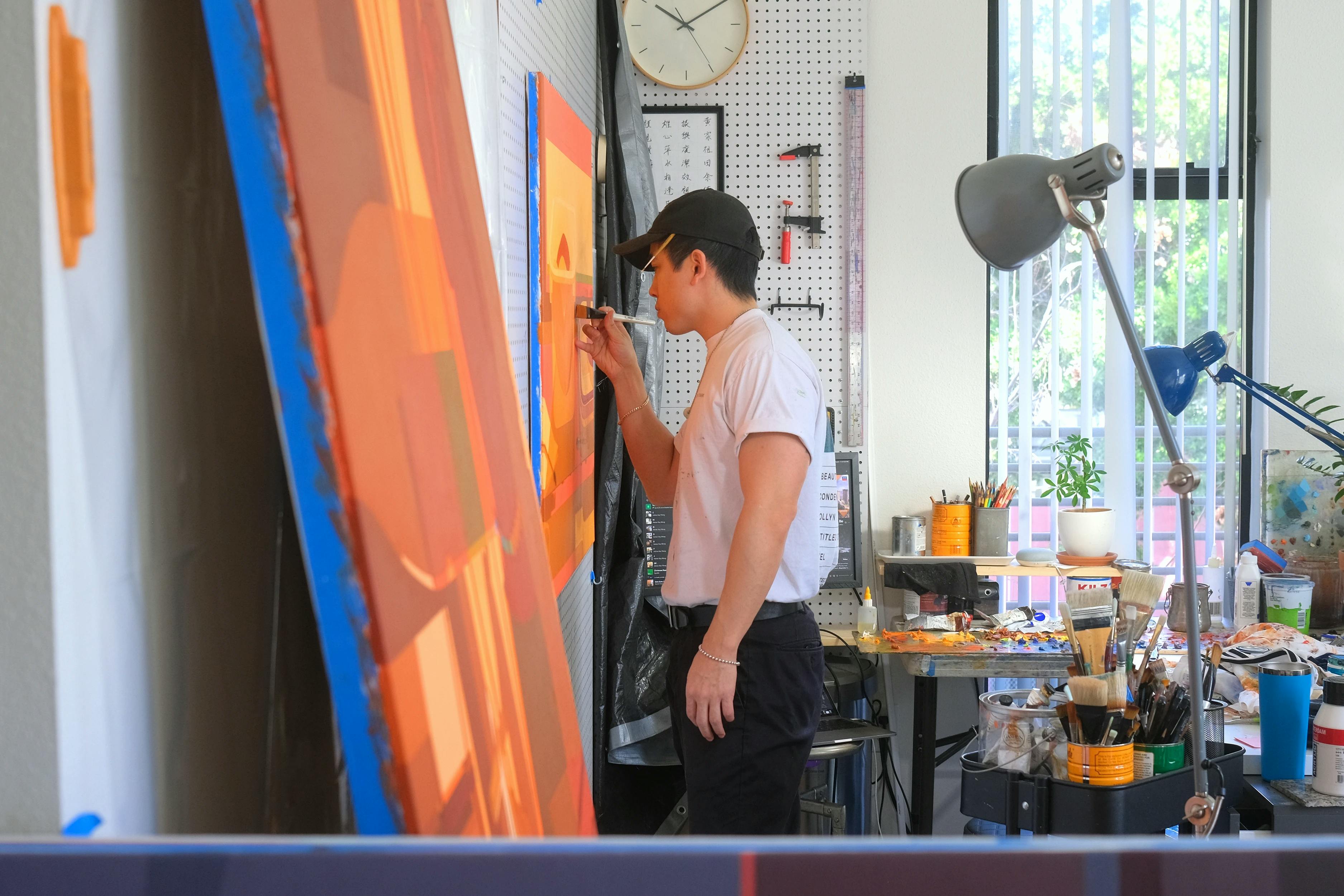 Artist Adrian Kay Wong painting an orange painting in his studio. 