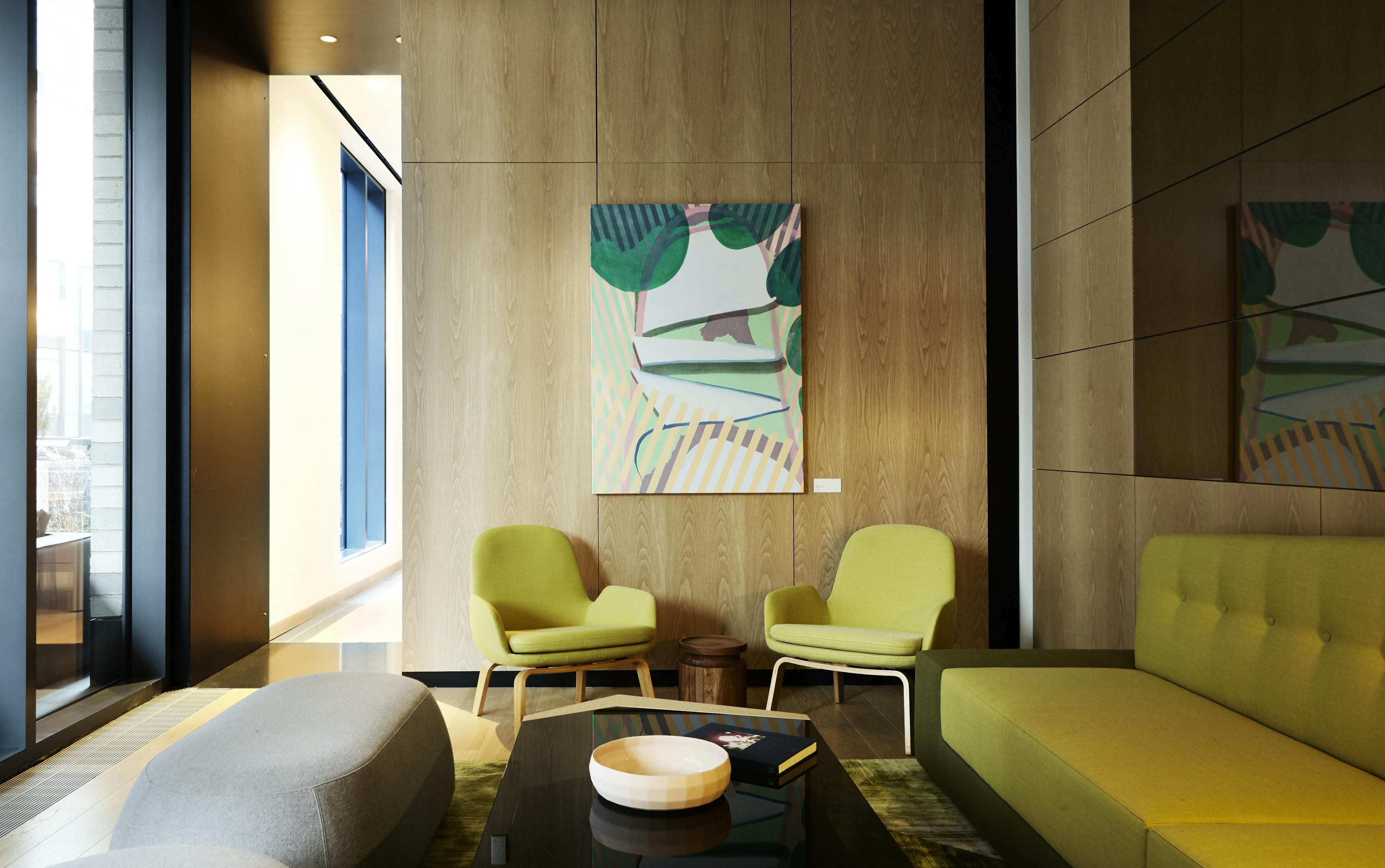 Green abstract painting with striated lines by artist Amelia Midori Miller on a wood wall within a lounge area with lime green arm chairs and a lime green sofa.