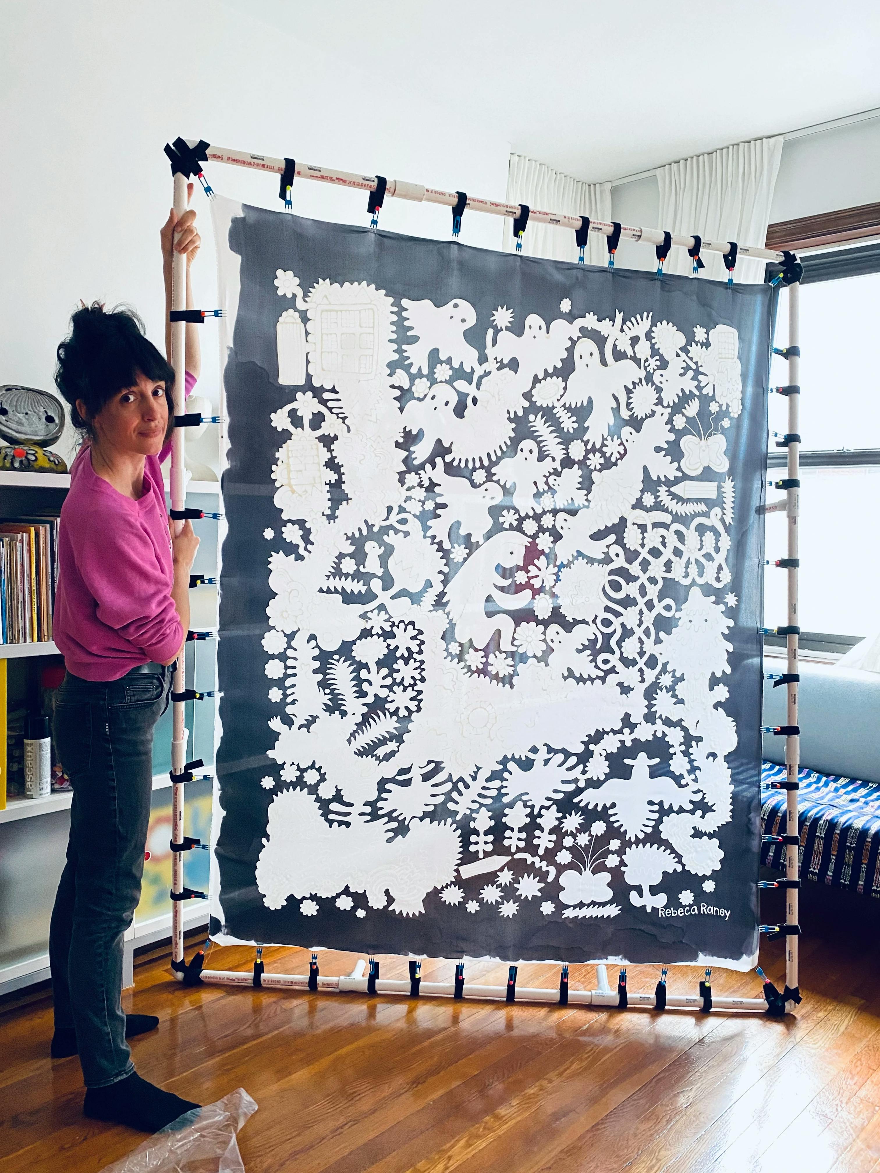 Artist Rebeca Raney holding up a stretched artwork on silk.