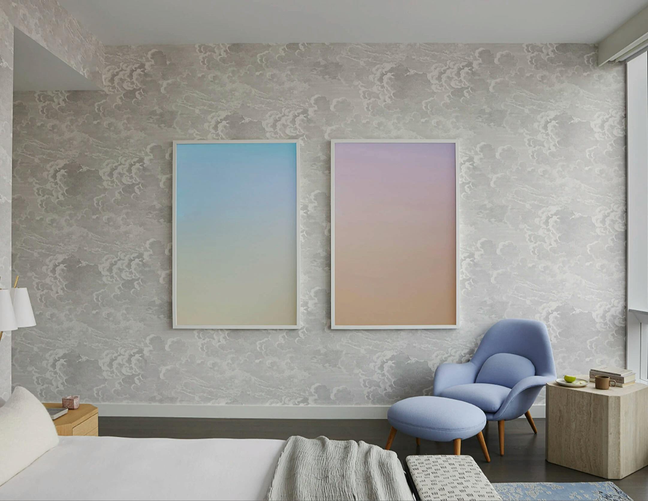 Two large photographs of pastel-colored skies by artist Jordan Sullivan installed side-by-side on a gray bedroom wall with a purple reading chair in the corner.