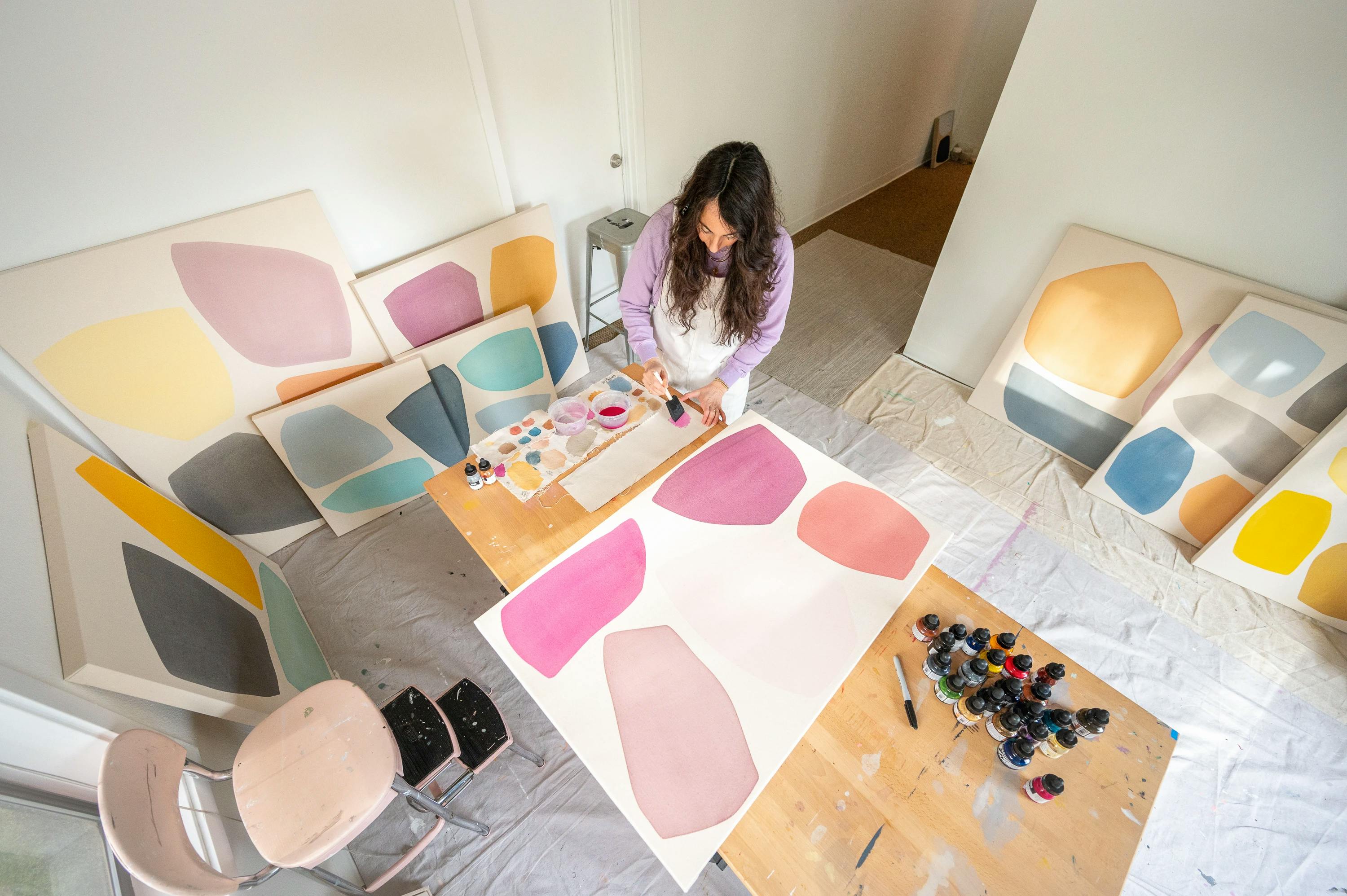 Artist Mia Farrington in her studio surrounded by colorful painted canvases.