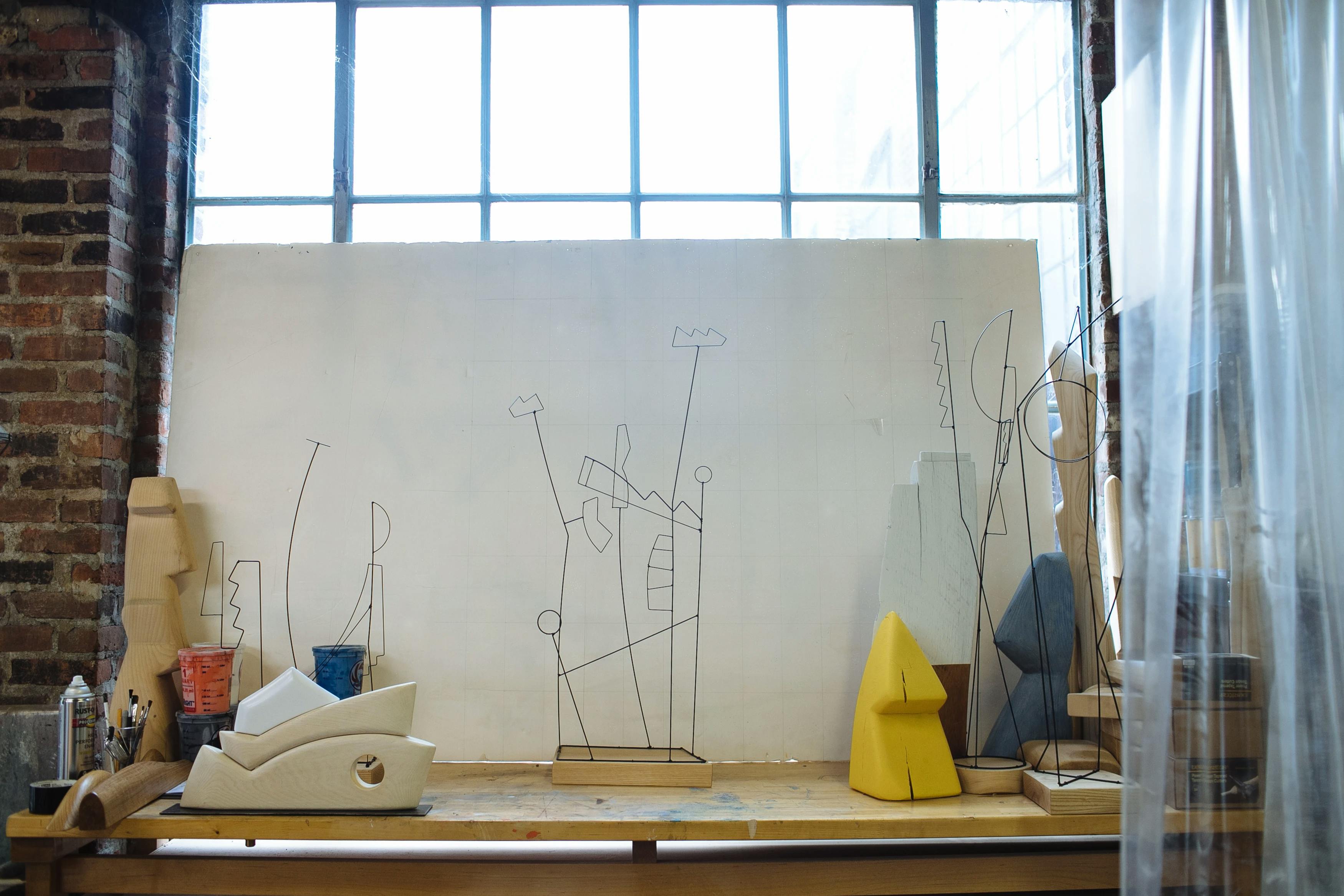 Three abstract wire sculptures on top of a wooden table in artist Fitzhugh Karol's workshop.