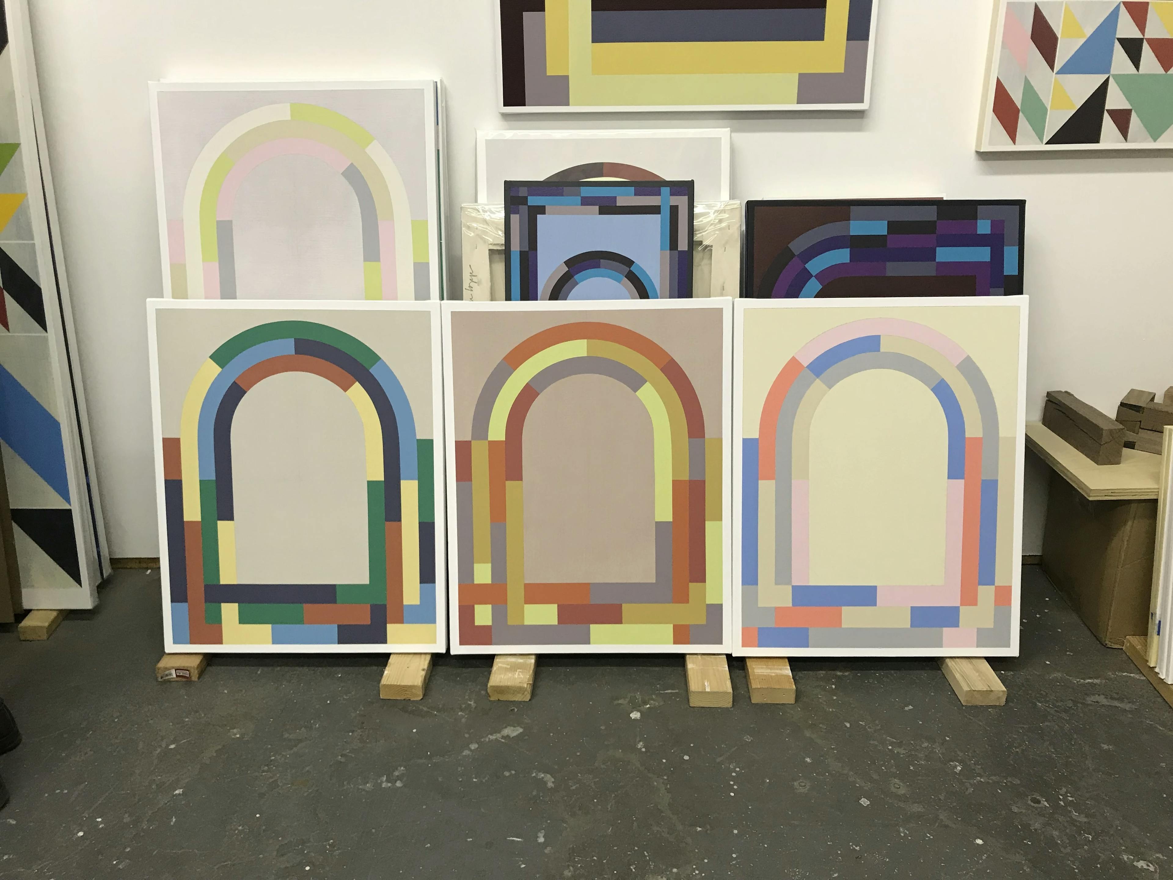 Arched, abstract geometric paintings by artist Christian Nguyen leaning on wooden planks in his studio.
