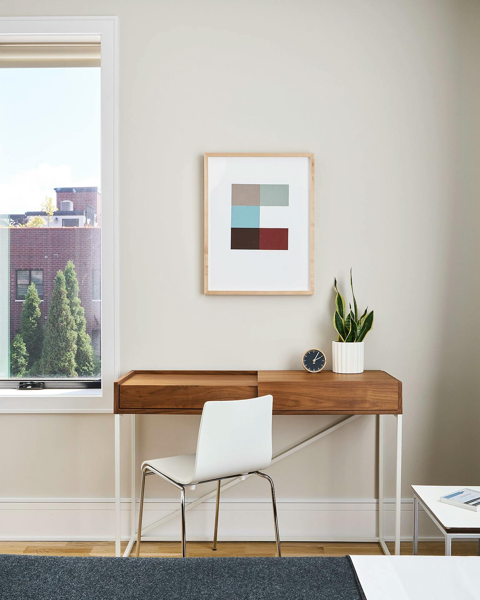 Framed geometric painting by artist Kristin Texeira installed on a white wall above a wooden desk with a white chair in a Chicago apartment.