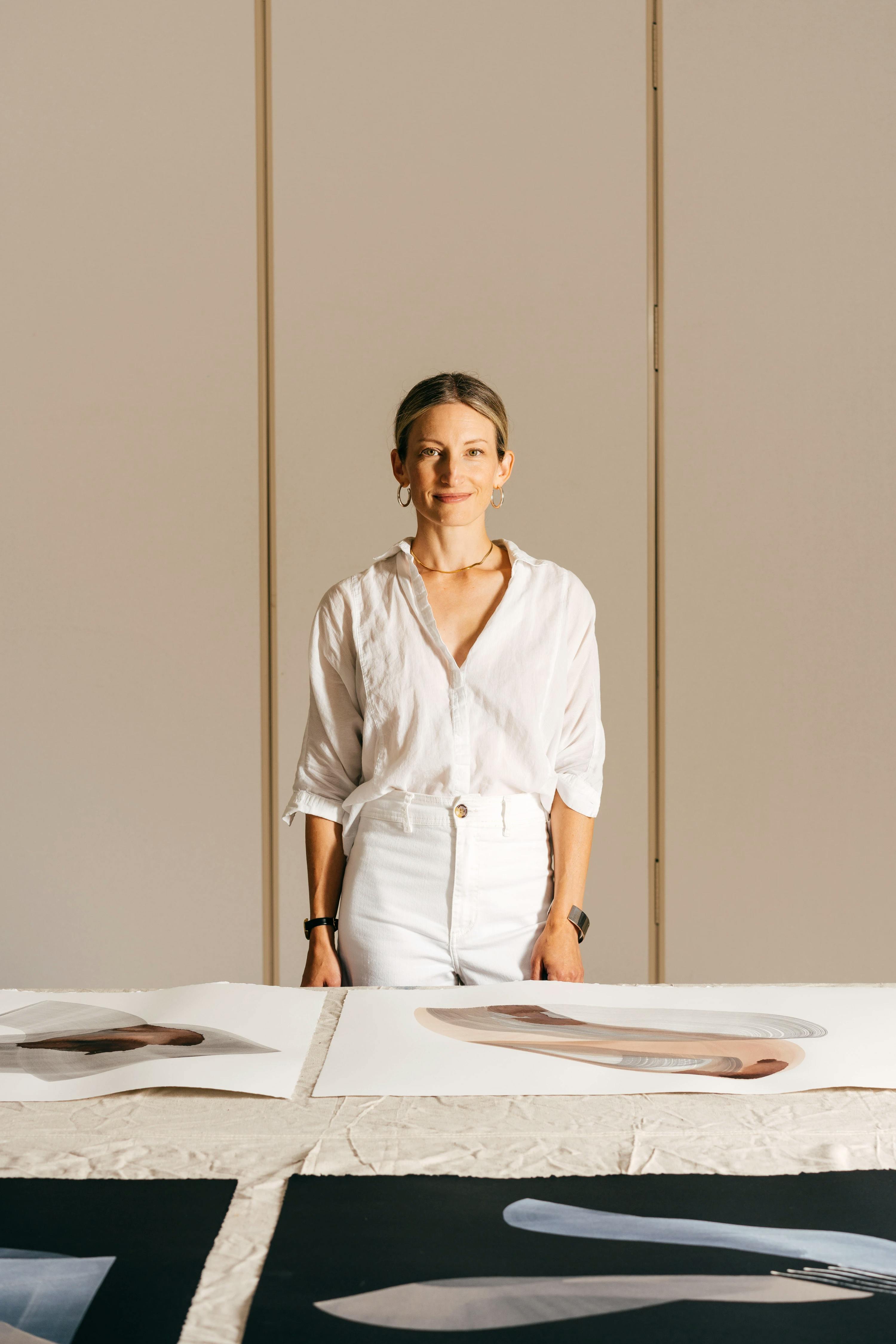 Artist Laura Naples stands behind large paintings on paper spread across a table at MacArthur Place.