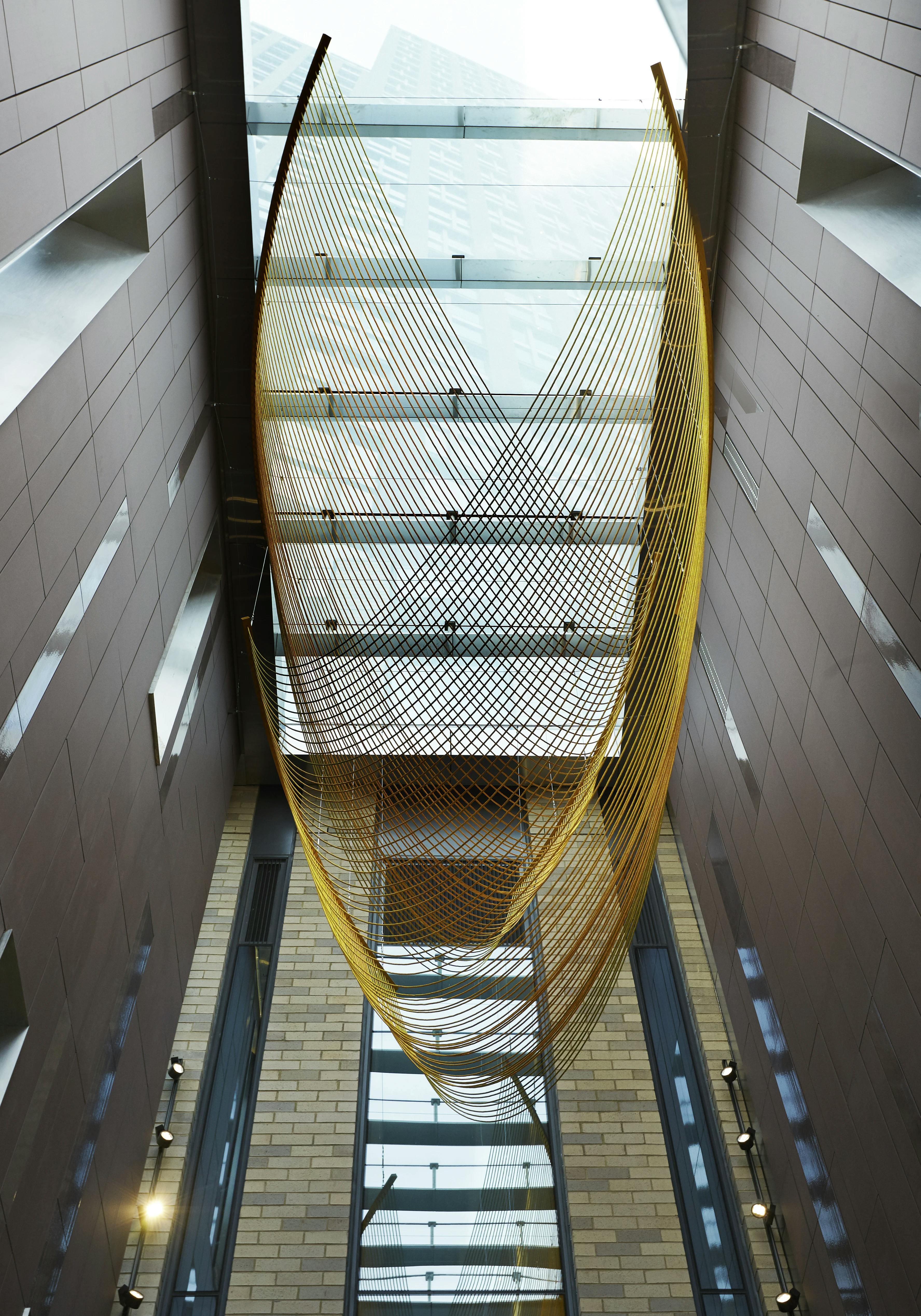 Large, site-specific installation of golden rope and steel by artist Rachel Mica Weiss suspended in the lobby of a modern building.