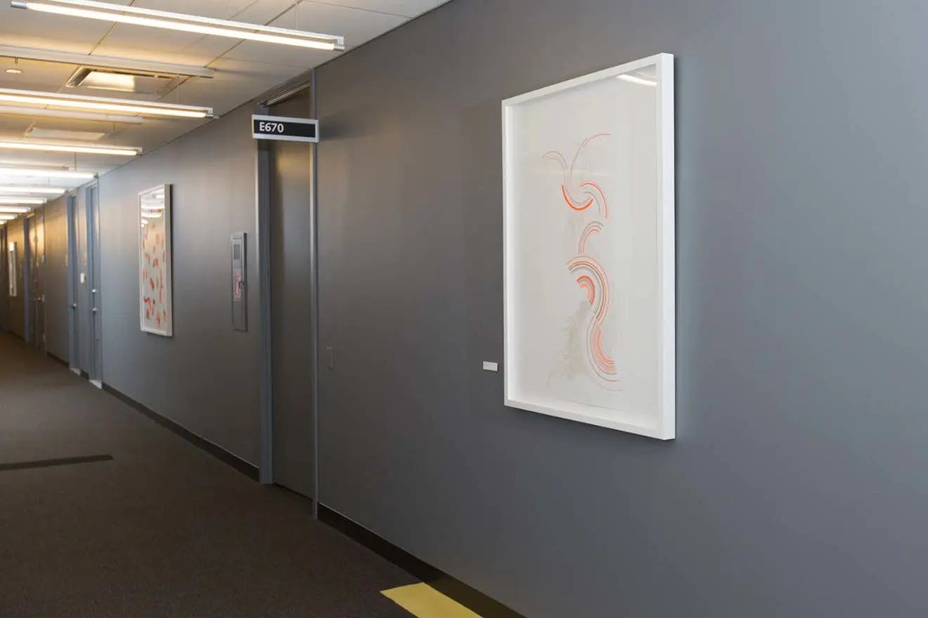 Framed artwork with colorful semicircles installed on a gray wall in the corridor of a modern office building.