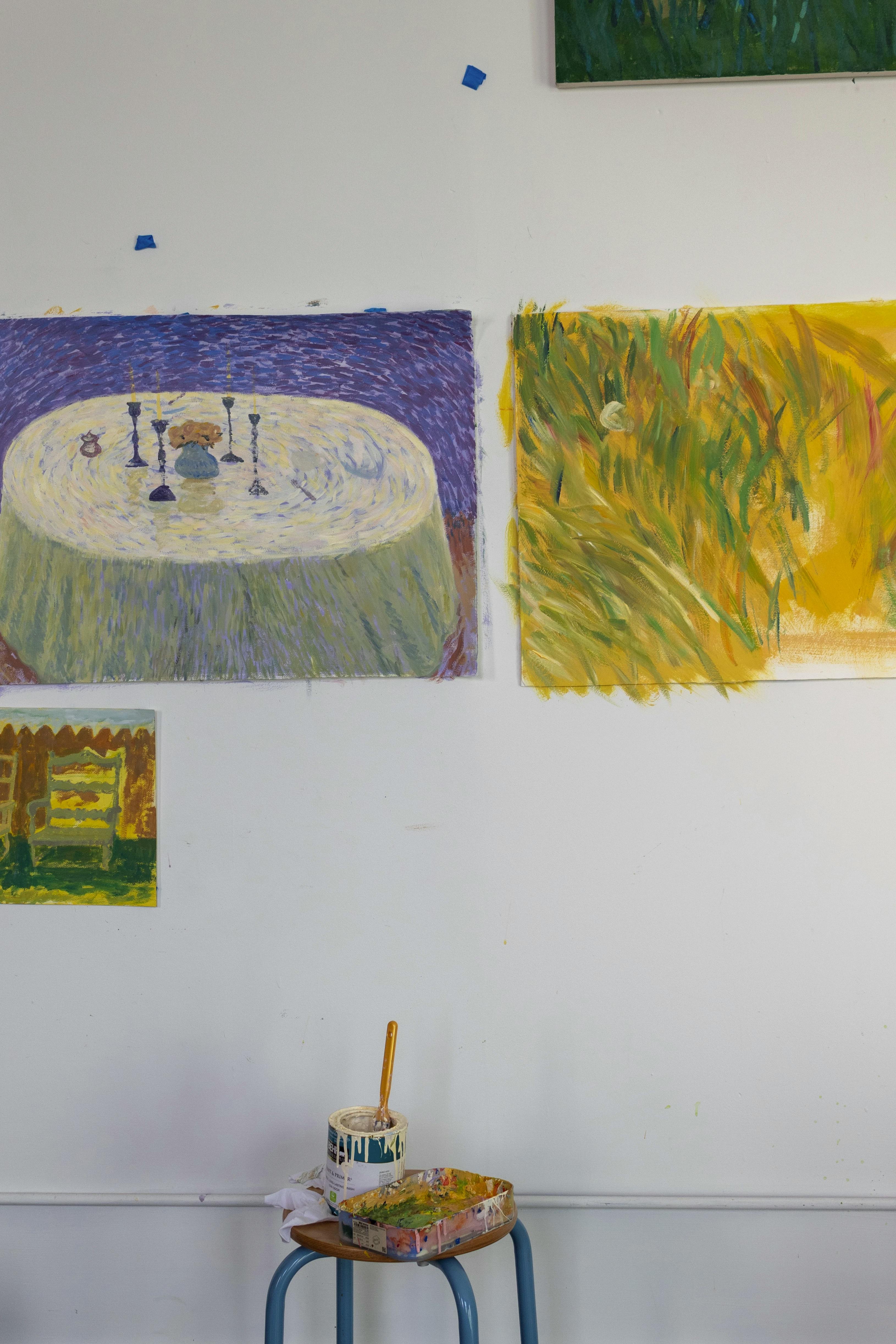 Three paintings of tablescapes and chairs by artist Jackson Joyce installed on a white wall in his studio.
