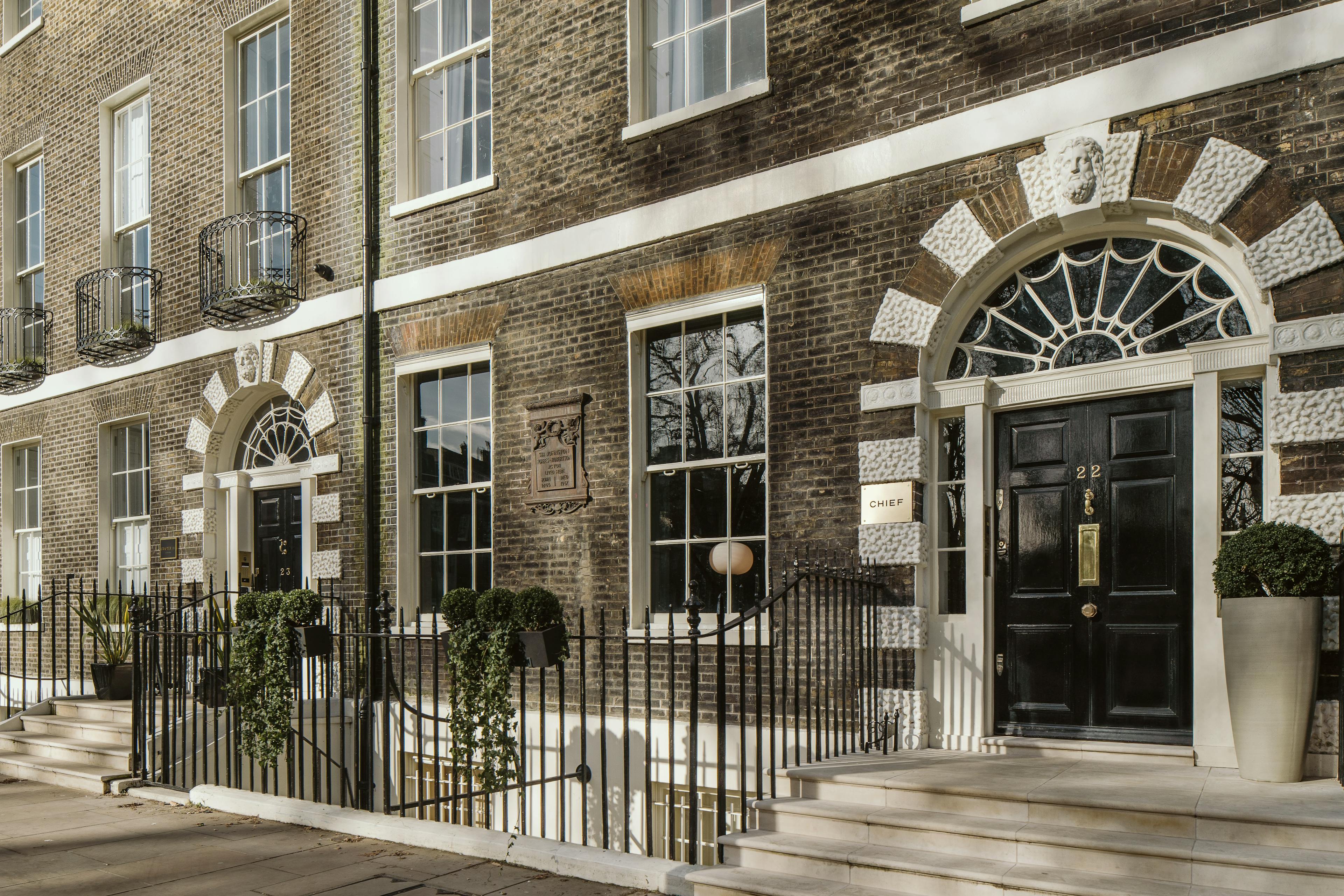 The outdoor brick facade of the Chief London clubhouse, featuring a gold sign inscribed with "CHIEF" and black door with a gold "22" on it.