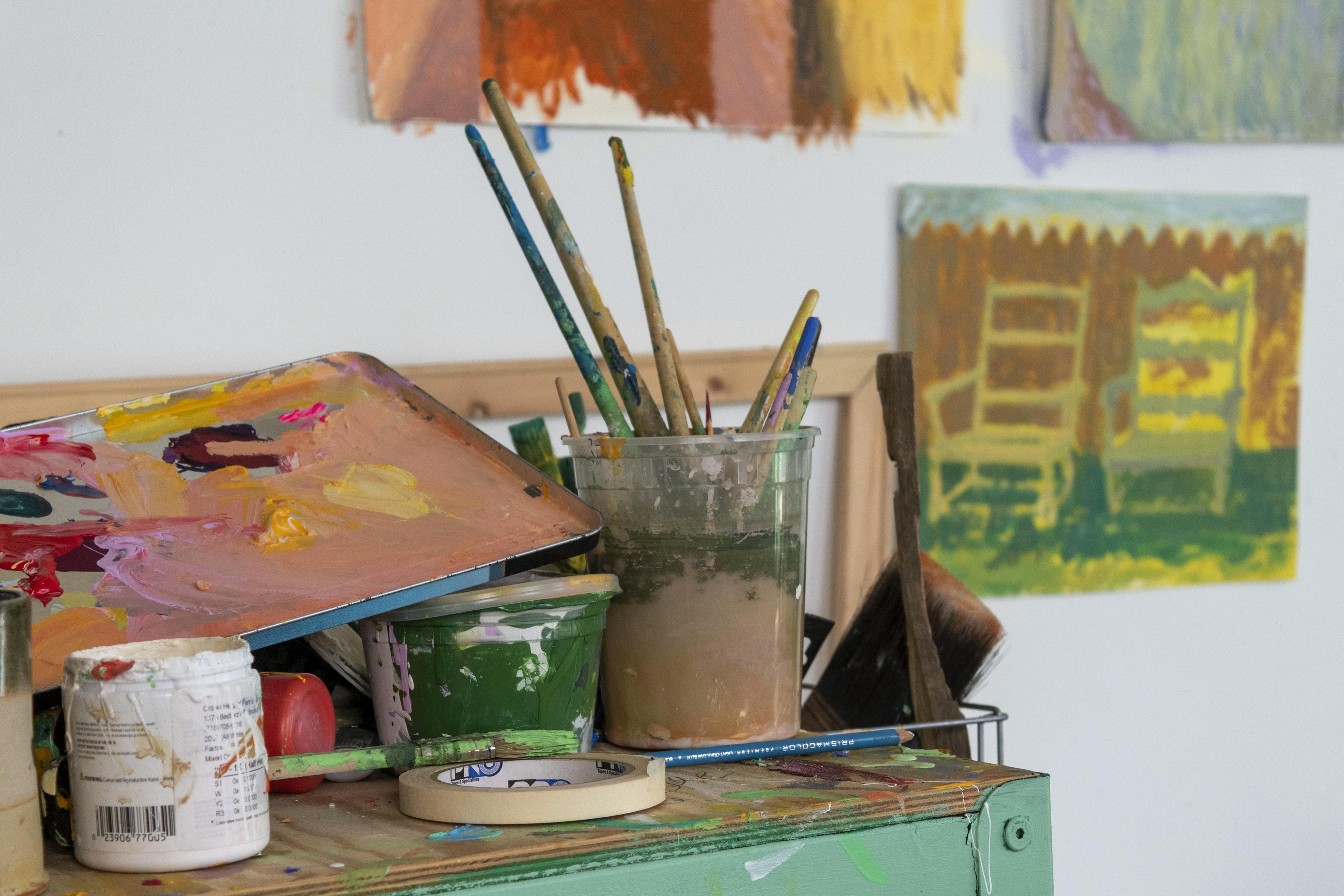 Brushes in cans, paint palettes, and masking tape on a wooden cart in artist Jackson Joyce's studio.