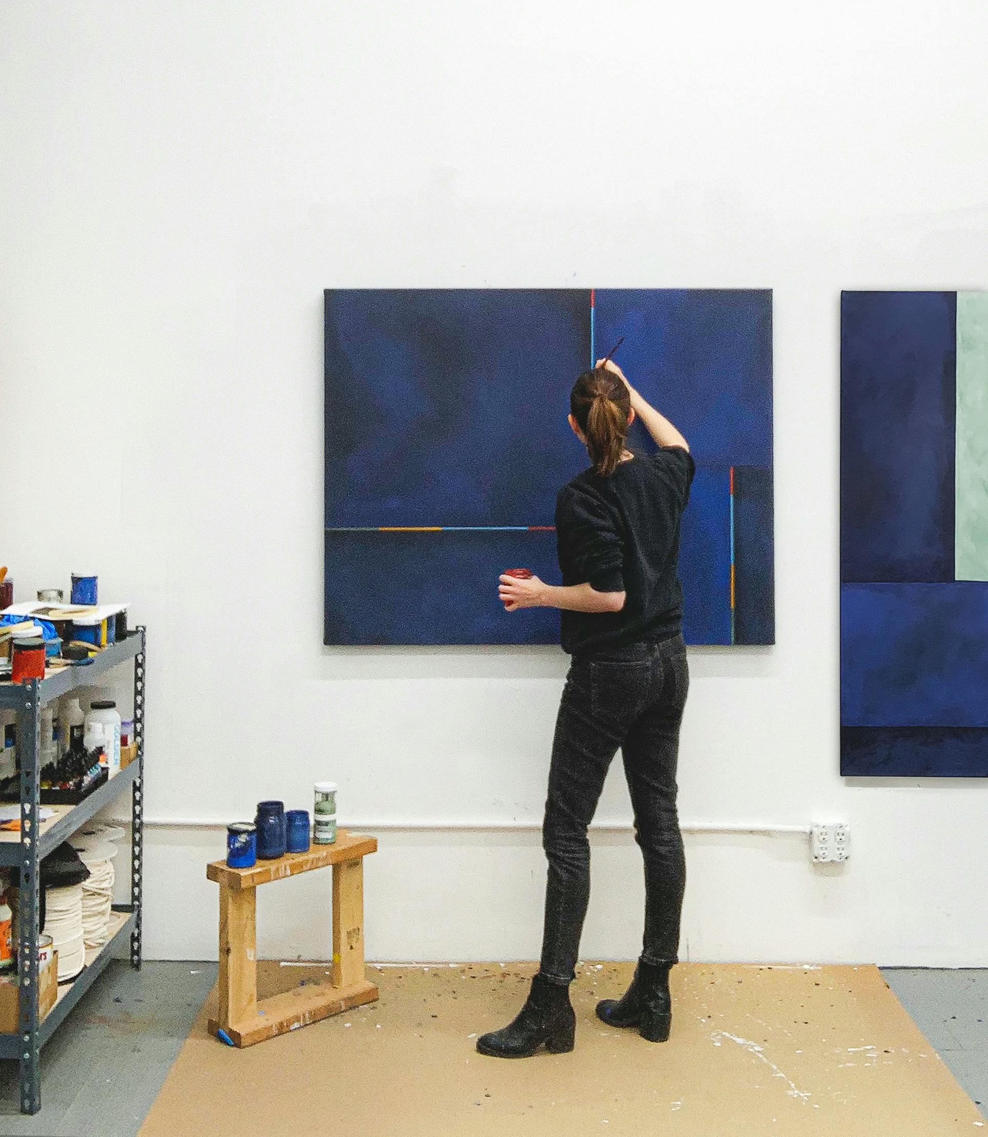 Artist Senem Oezdogan standing in her studio painting a monochrome dark blue painting.