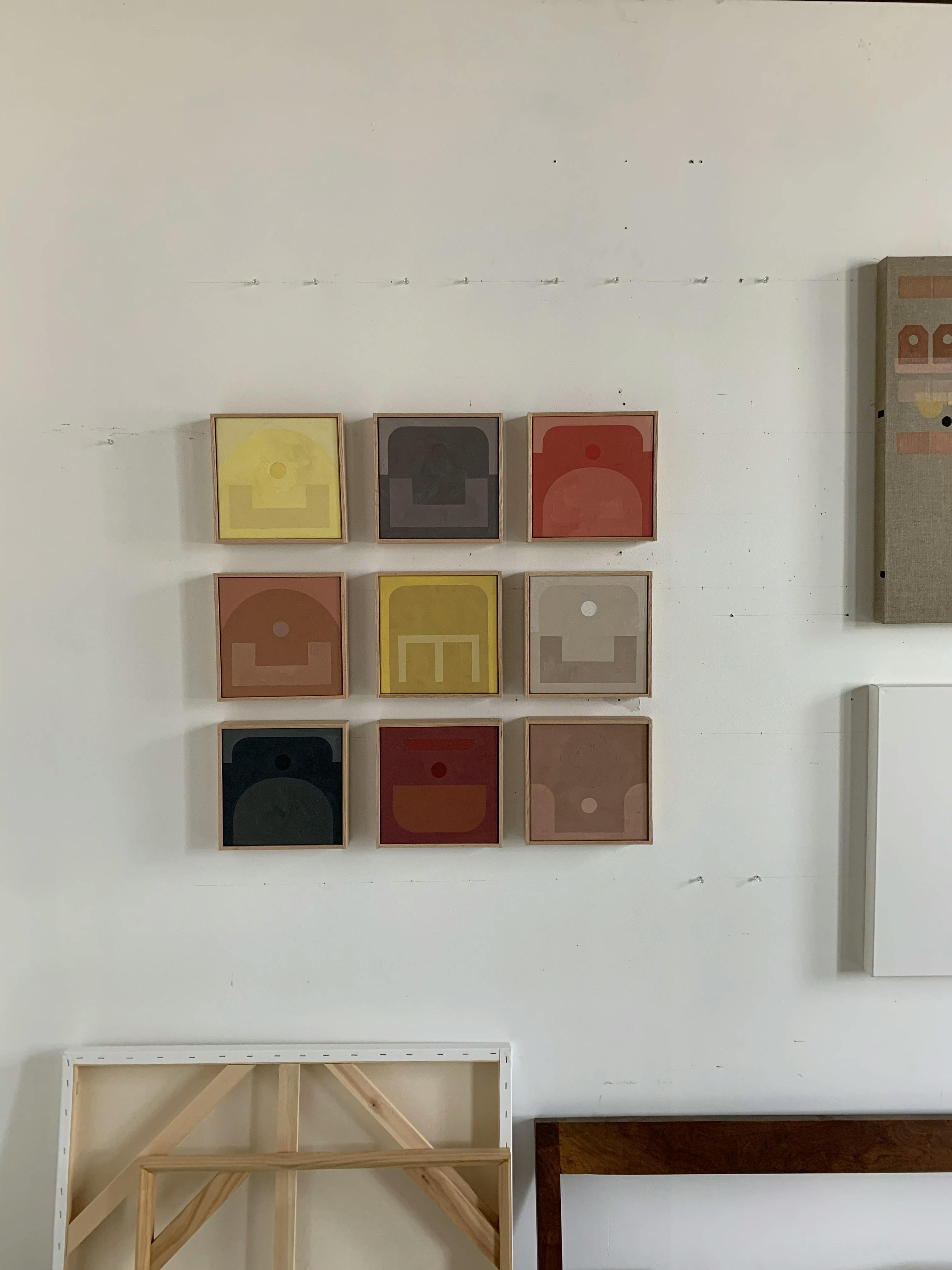 A grid of nine, small monochrome paintings by artist Carla Weeks installed on a white wall in her studio.