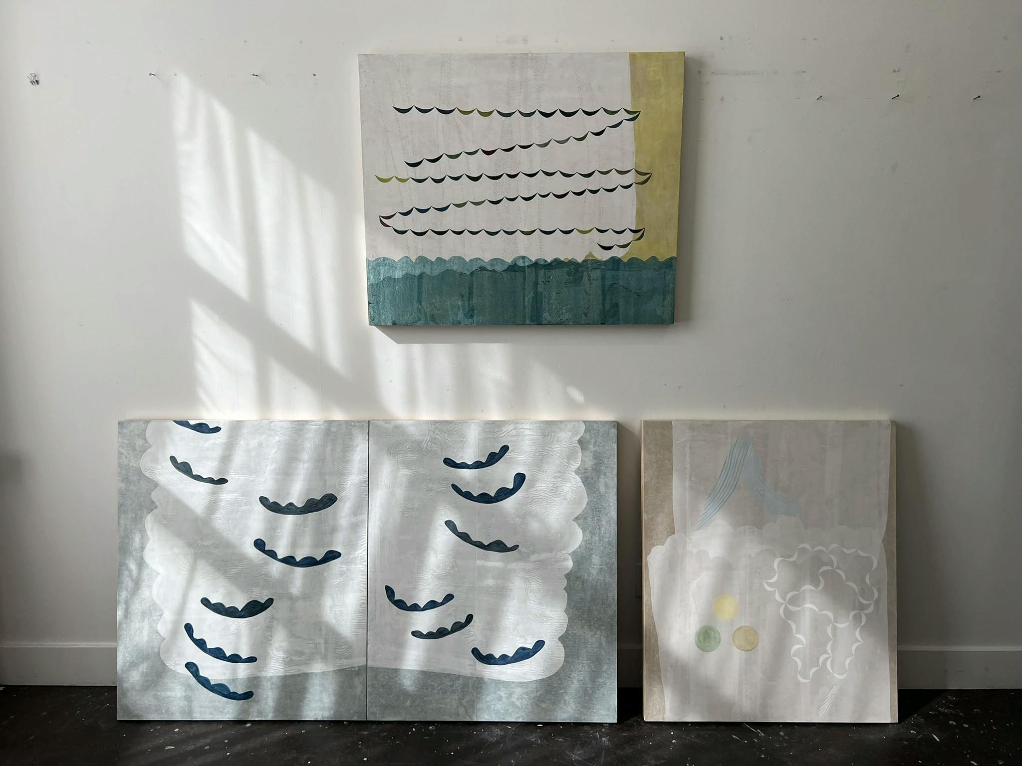 Light from windows casting shadows on three paintings by artist Lydia Bassis in her studio.