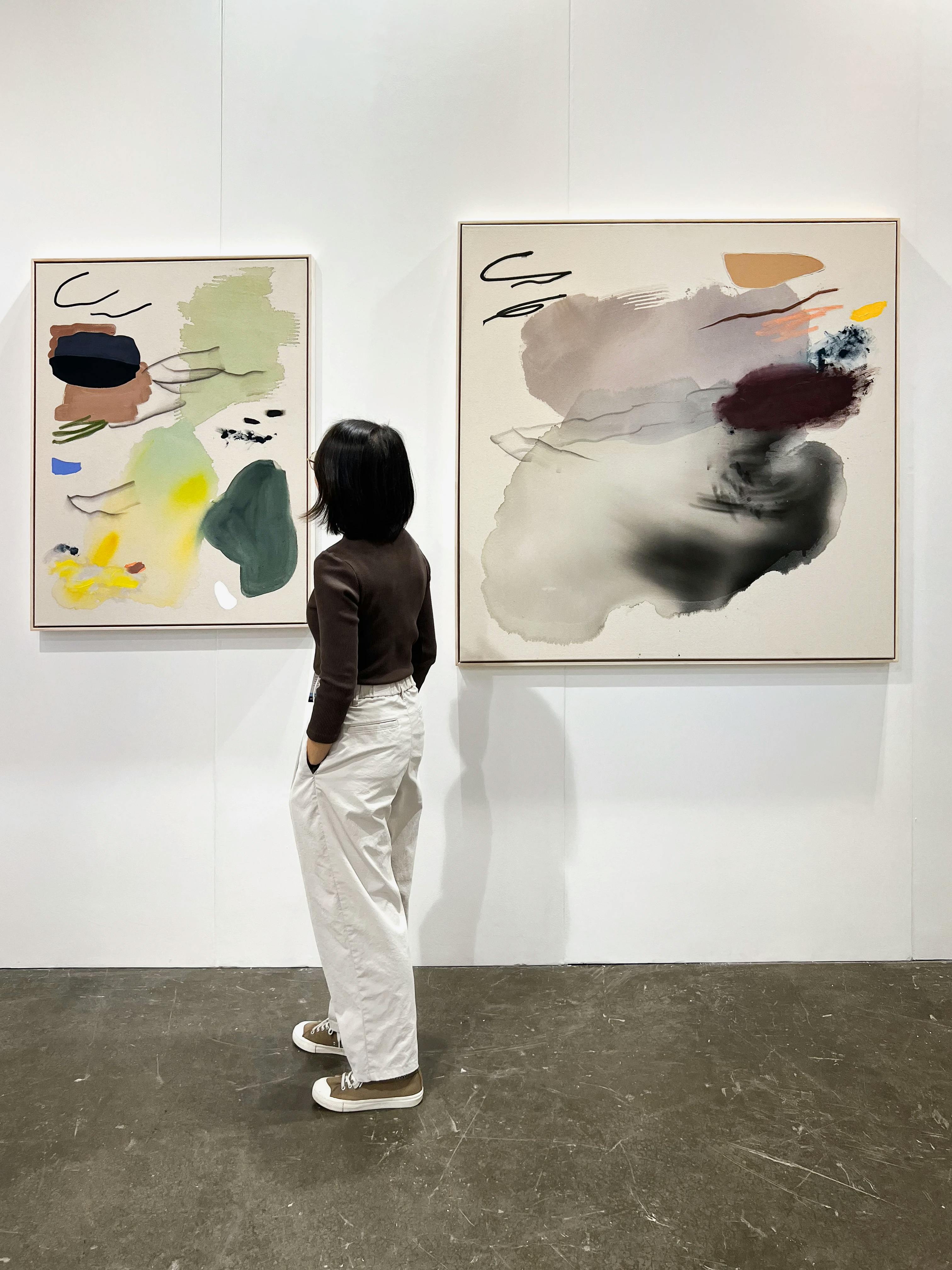 A person stands in front of paintings by Karina Bania at Art Central Hong Kong.