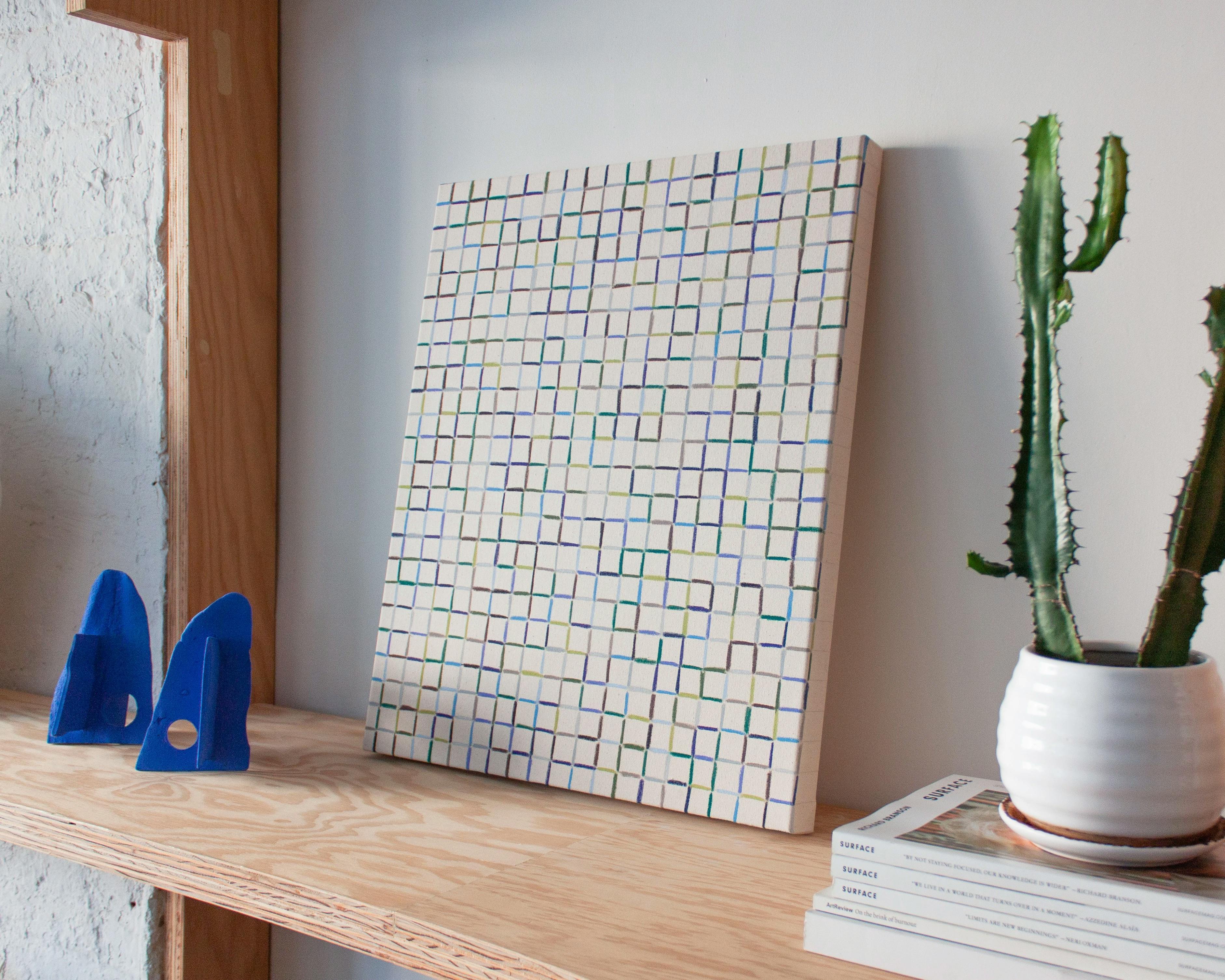 A blue and purple grid painting by Devon Reina leaning on wood shelf at Uprise Art.