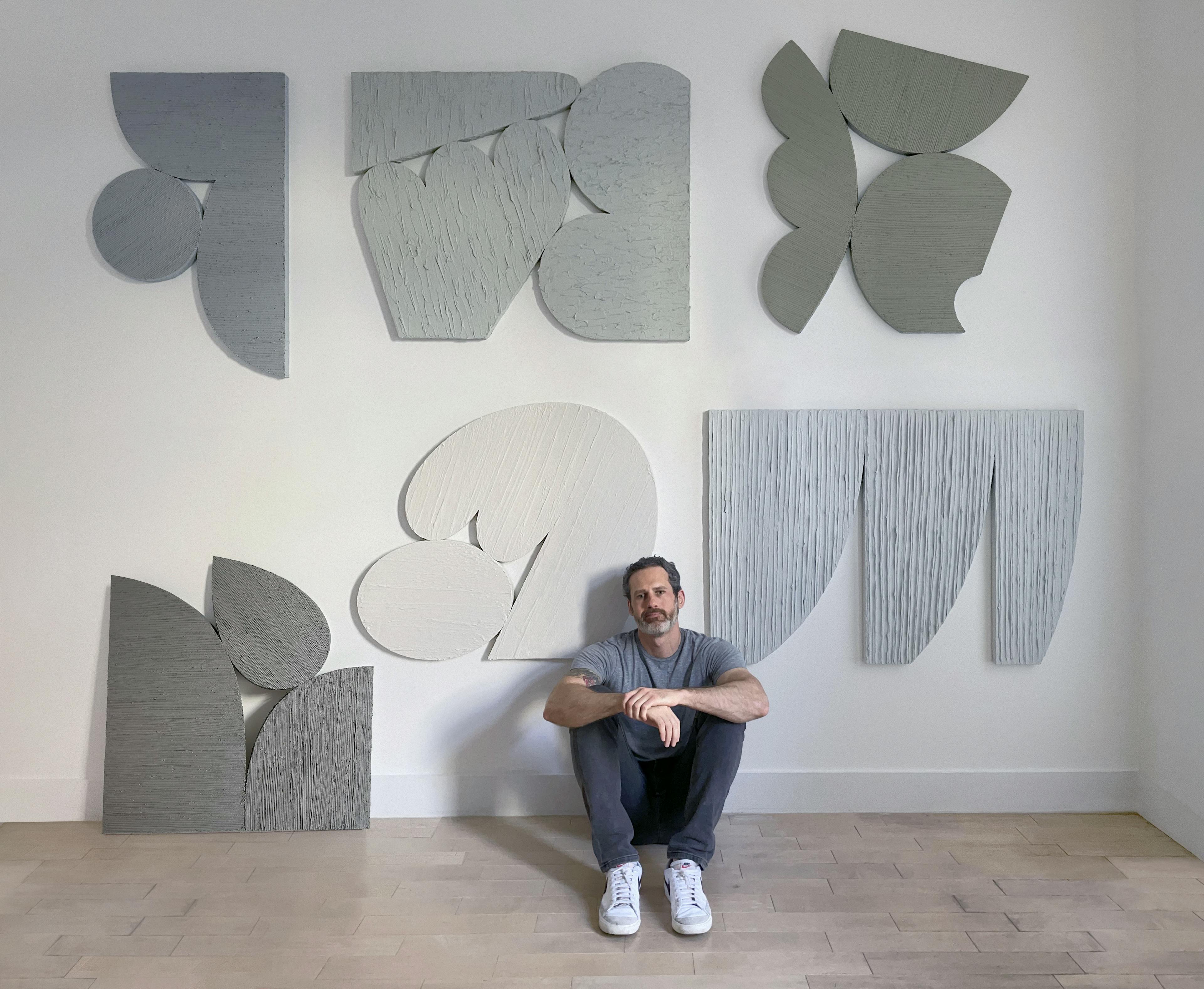 Artist Dan Covert sitting on the floor surrounded by his textural wall-based works.