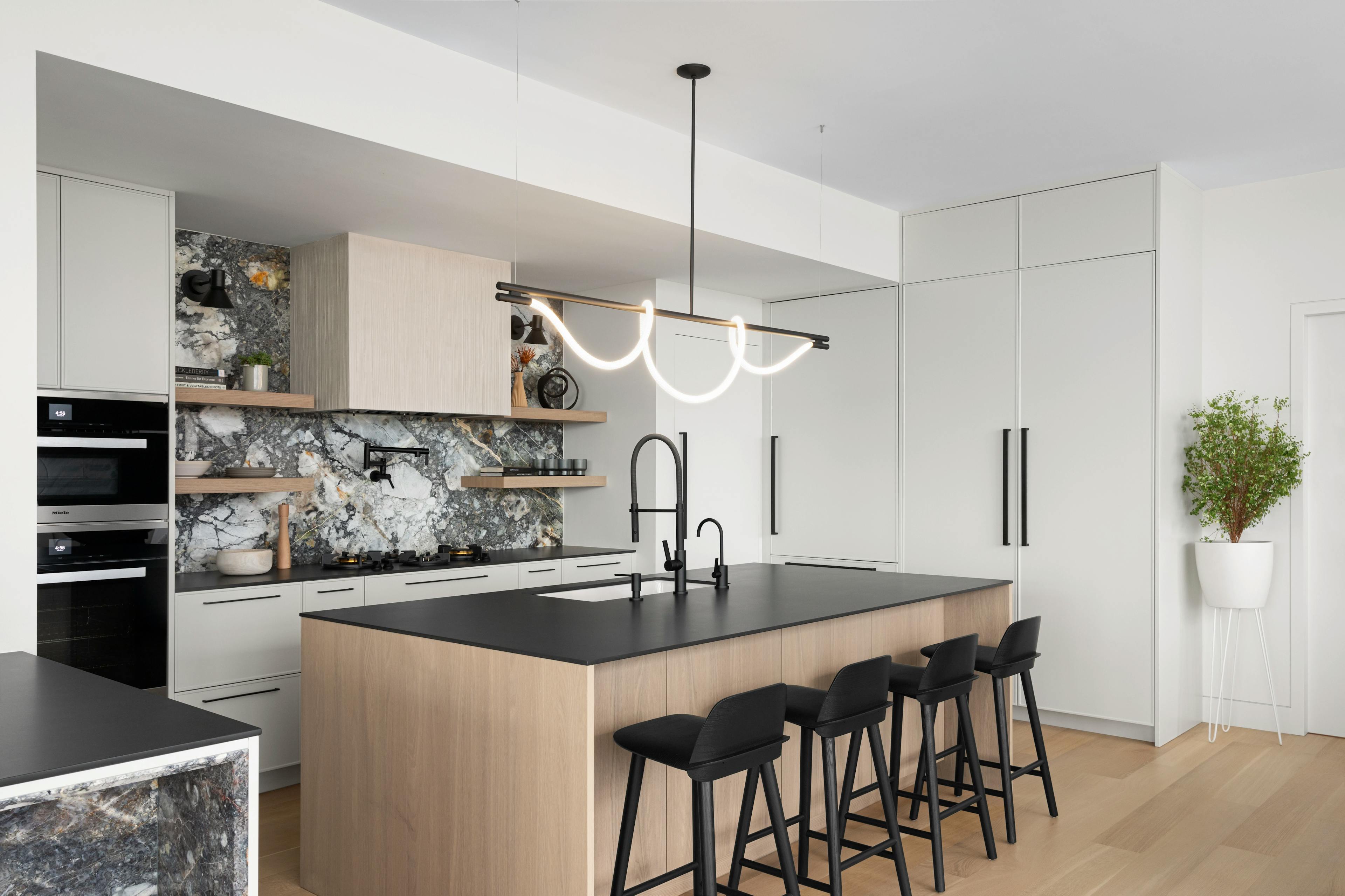 Modern kitchen with a large beige island, black kitchen stools, and marbled granite backsplash in a Brooklyn apartment.