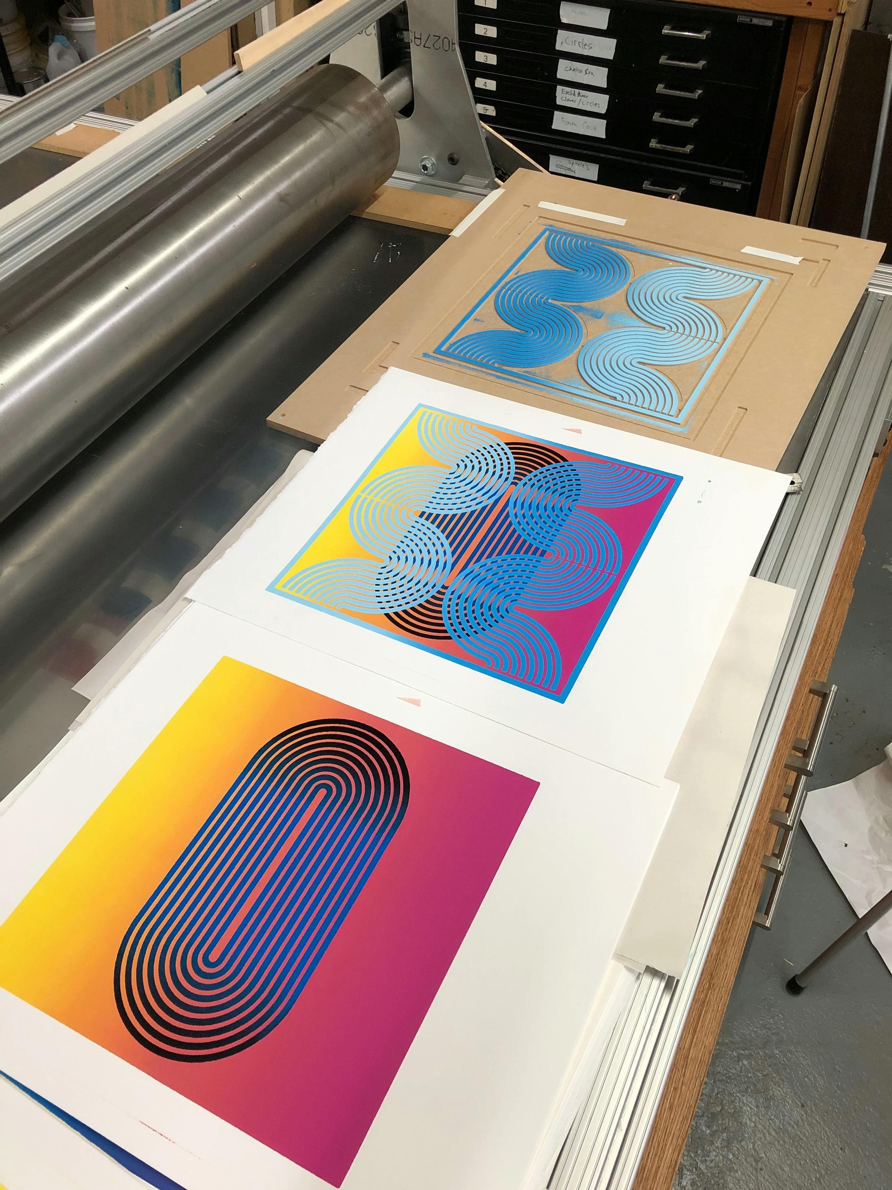 Colorful woodblock prints by artist Matt Neuman laying on top of an etching press in his studio.
