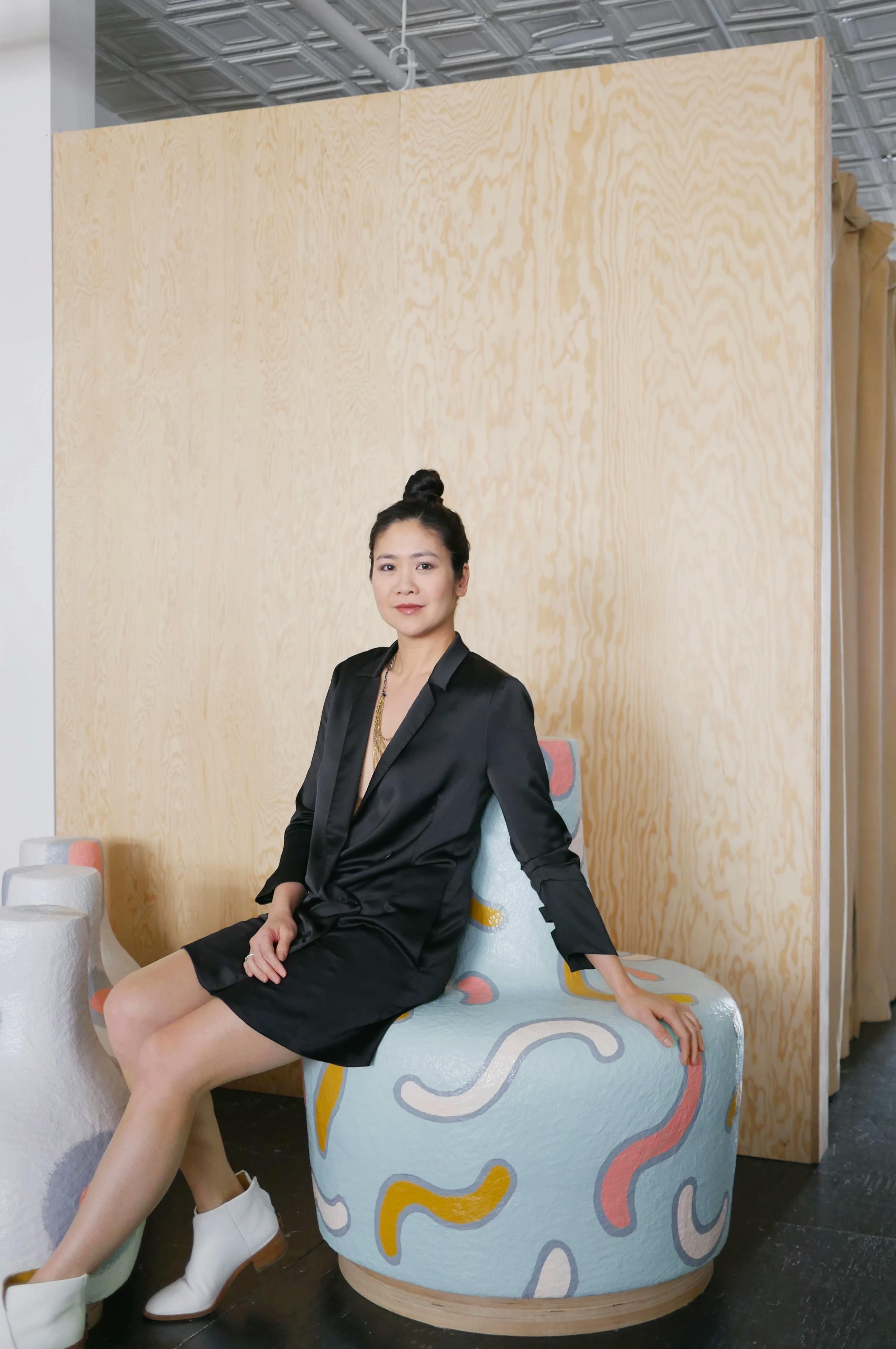 Portrait of founder Tze Chun sitting on a blue chair in front of a wood wall at Uprise Art.