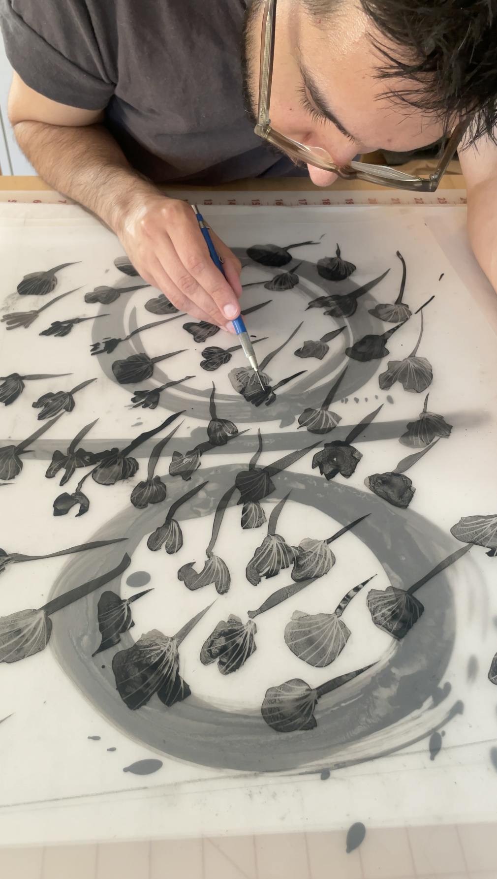 Artist Ruben Castillo using a thin paintbrush to paint black, repeating floral motifs on translucent paper.