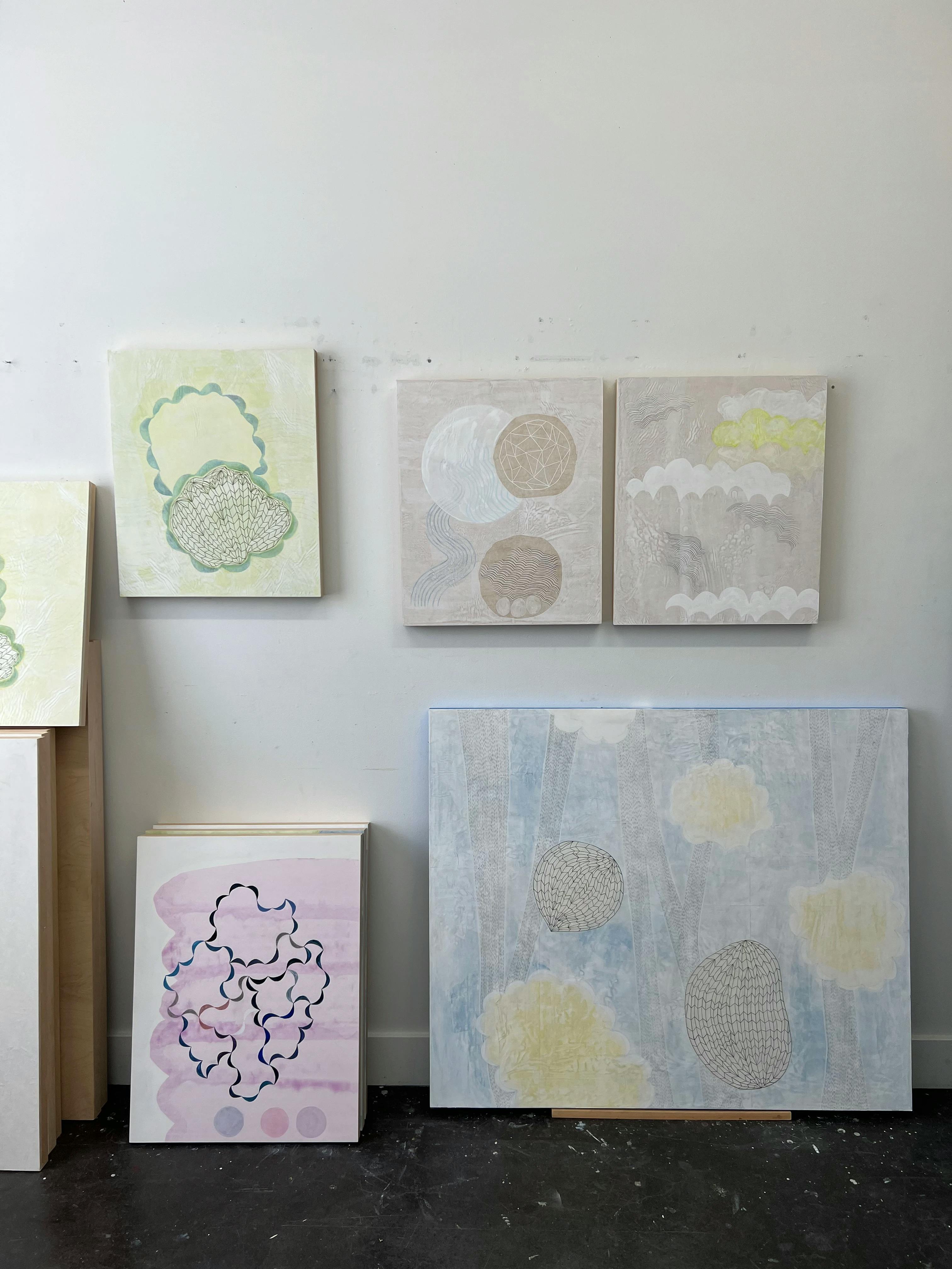 Pastel-colored abstract paintings with water motifs by artist Lydia Bassis installed and leaning against a white wall in her studio.
