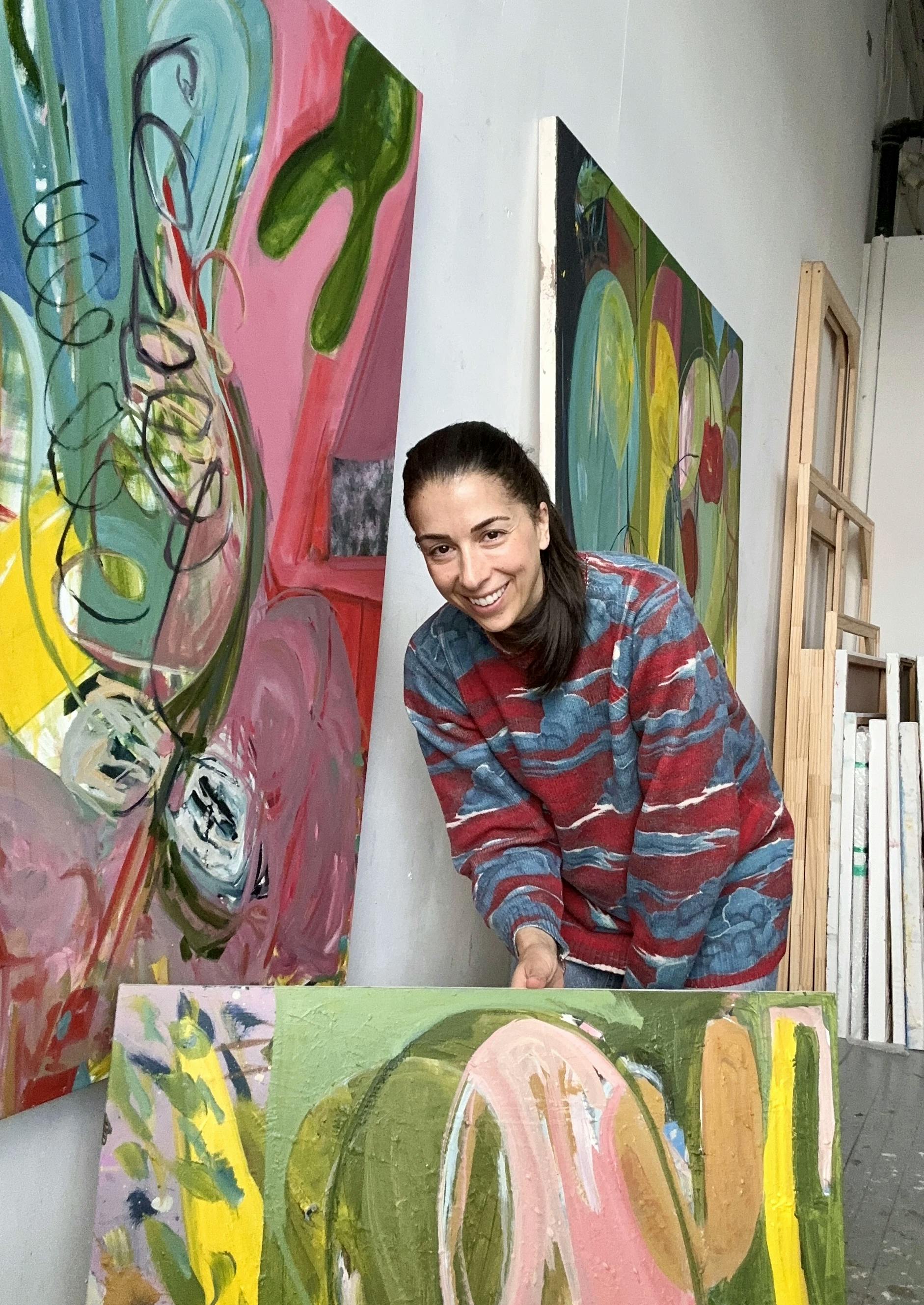 Artist Diana Delgado in the studio standing amongst her colorful, gestural abstract paintings.