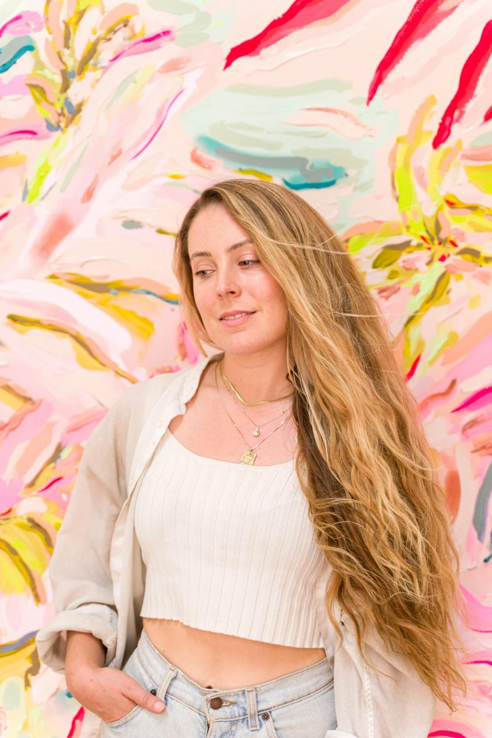Artist Erin Lynn Welsh standing in front of a pink floral painting. 